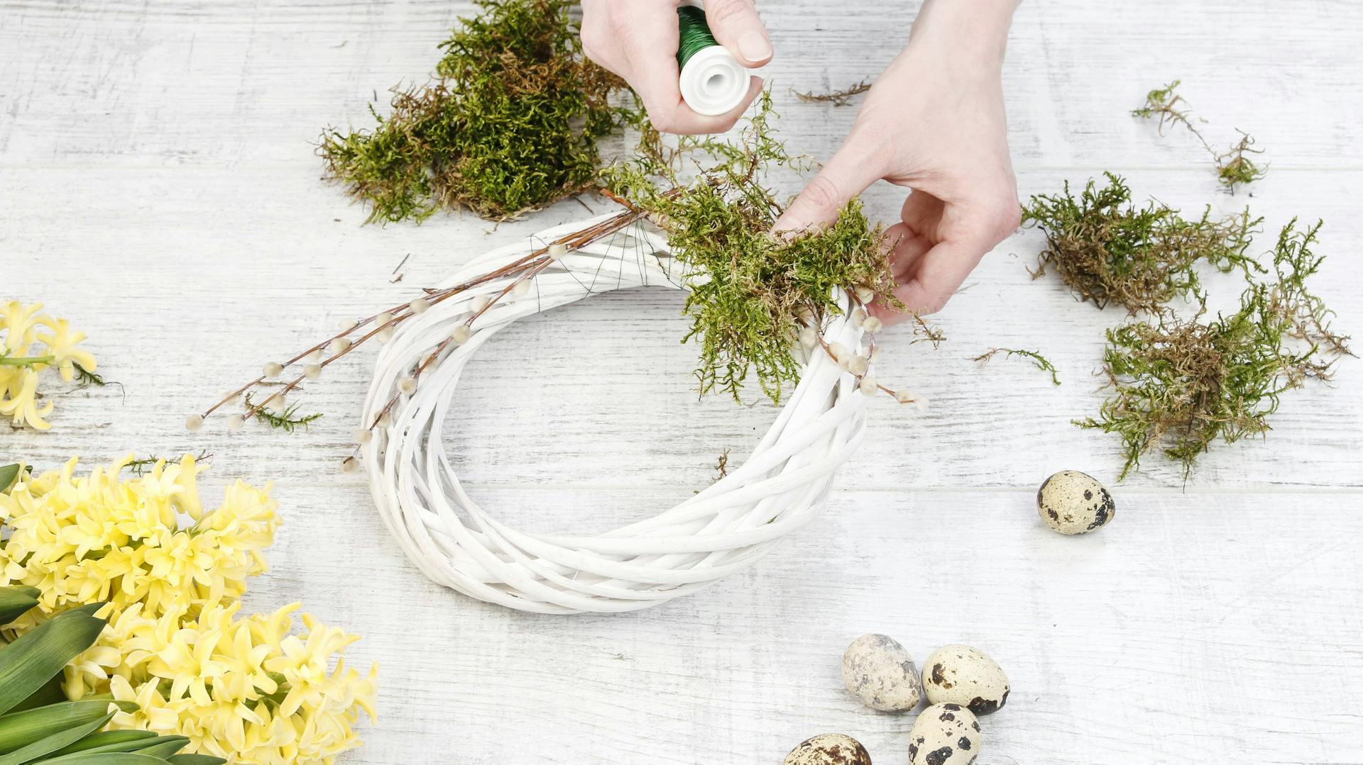 Jemand bindet einen Osterkranz mit Moos