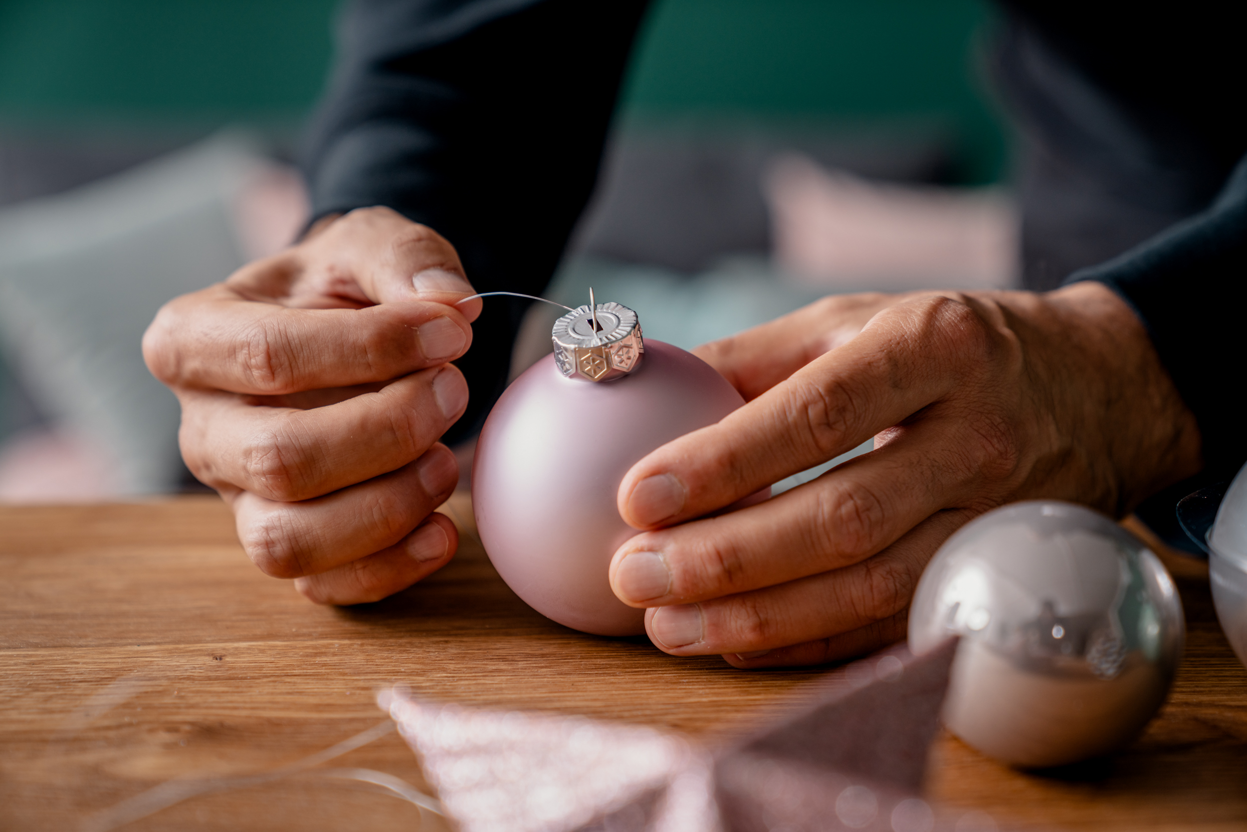 Dünne Nylonfäden werden durch den Aufhänger einer rosa Weihnachtskugel gefädelt.