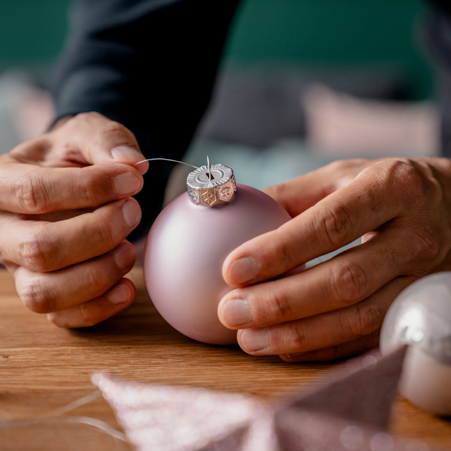 Dünne Nylonfäden werden durch den Aufhänger einer rosa Weihnachtskugel gefädelt.