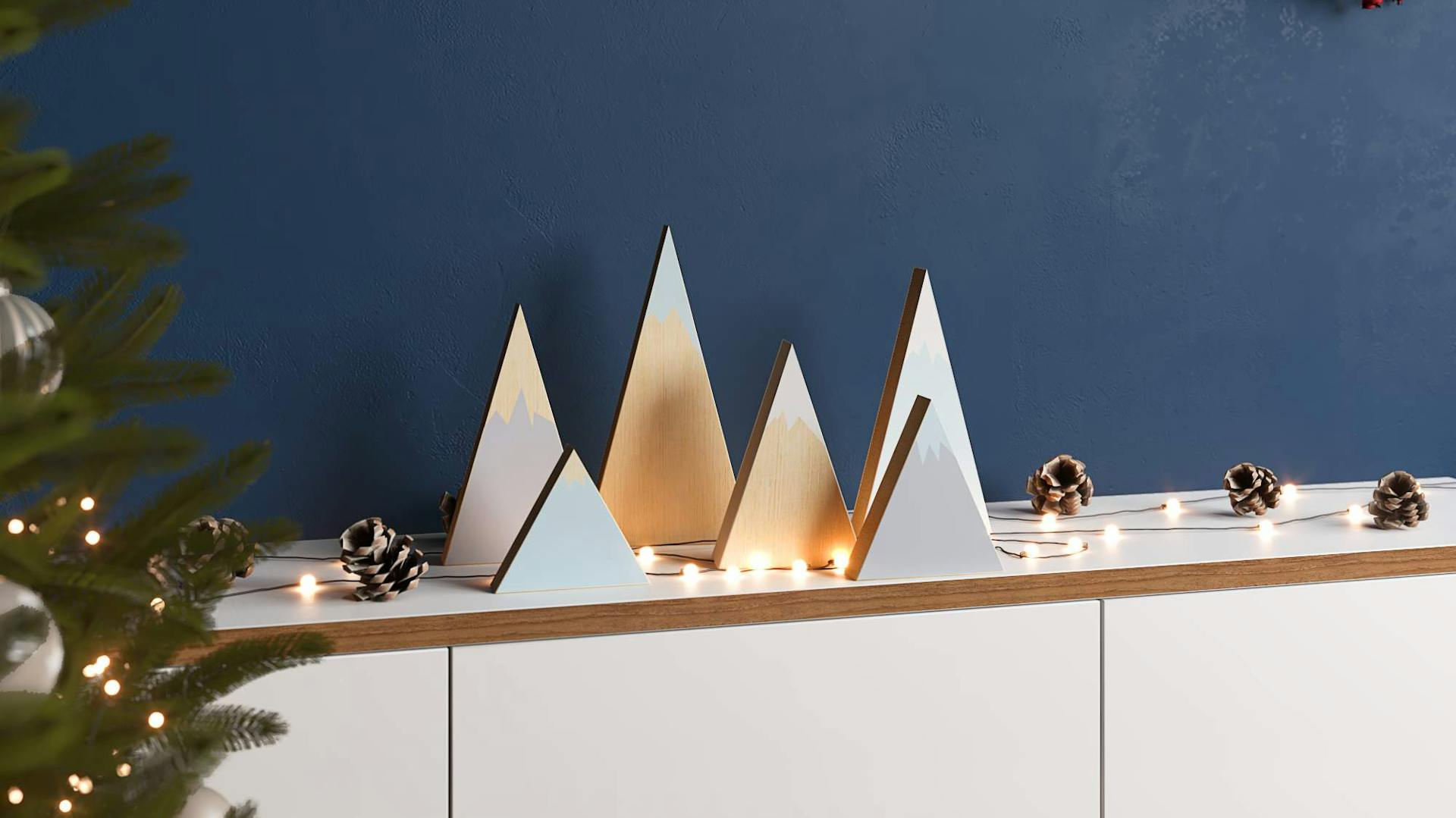 Kleiner bemalter Tannenwald aus Holz mit Lichterkette auf Sideboard neben Weihnachtsbaum