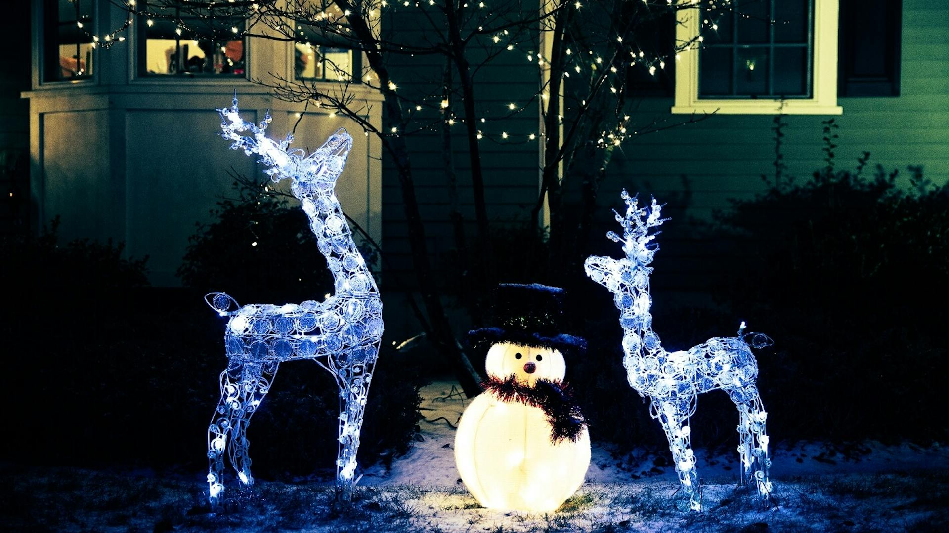 Due renne e un pupazzo di neve come figura luminosa nel giardino innevato