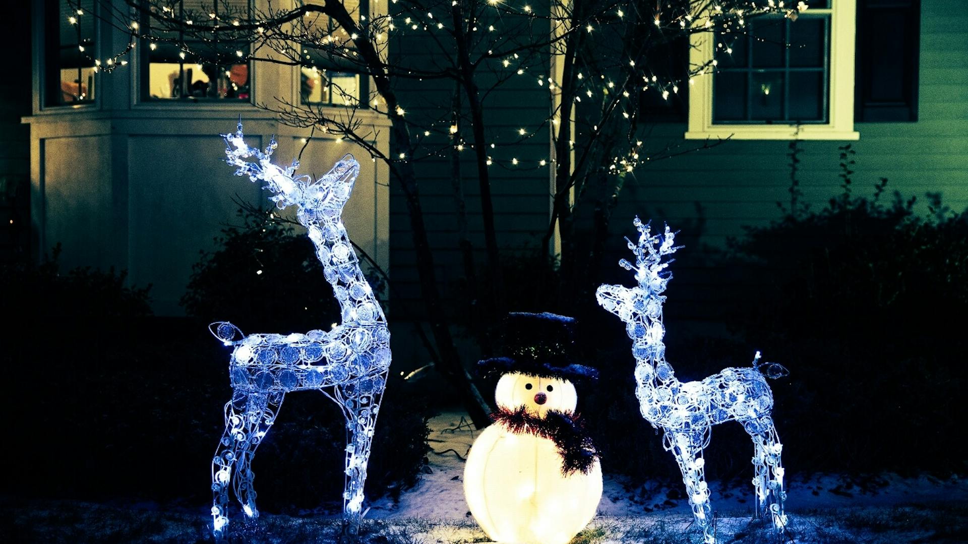 Zwei Rentiere und ein Schneemann als Leuchtfigur im schneebedeckten Garten