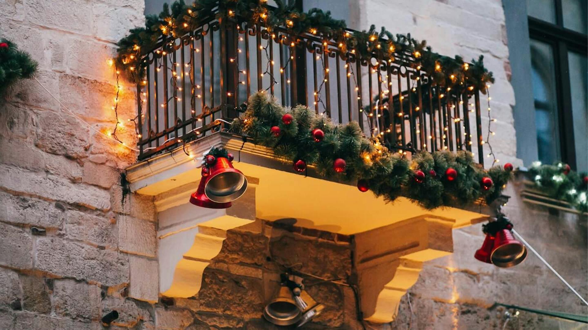 Ringhiera da balcone avvolta in ramoscelli d’abete e illuminata con ghirlande luminose.
