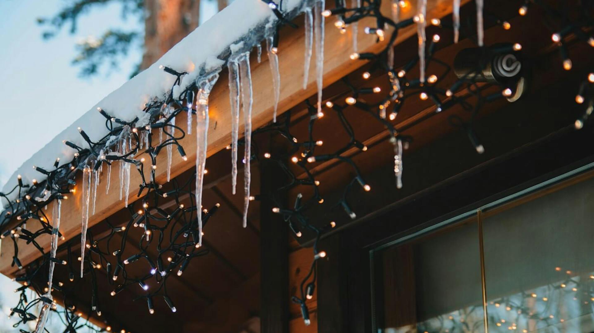 Bordo esterno di un tetto innevato con ghiaccioli. Su di esso è collocata una ghirlanda luminosa.