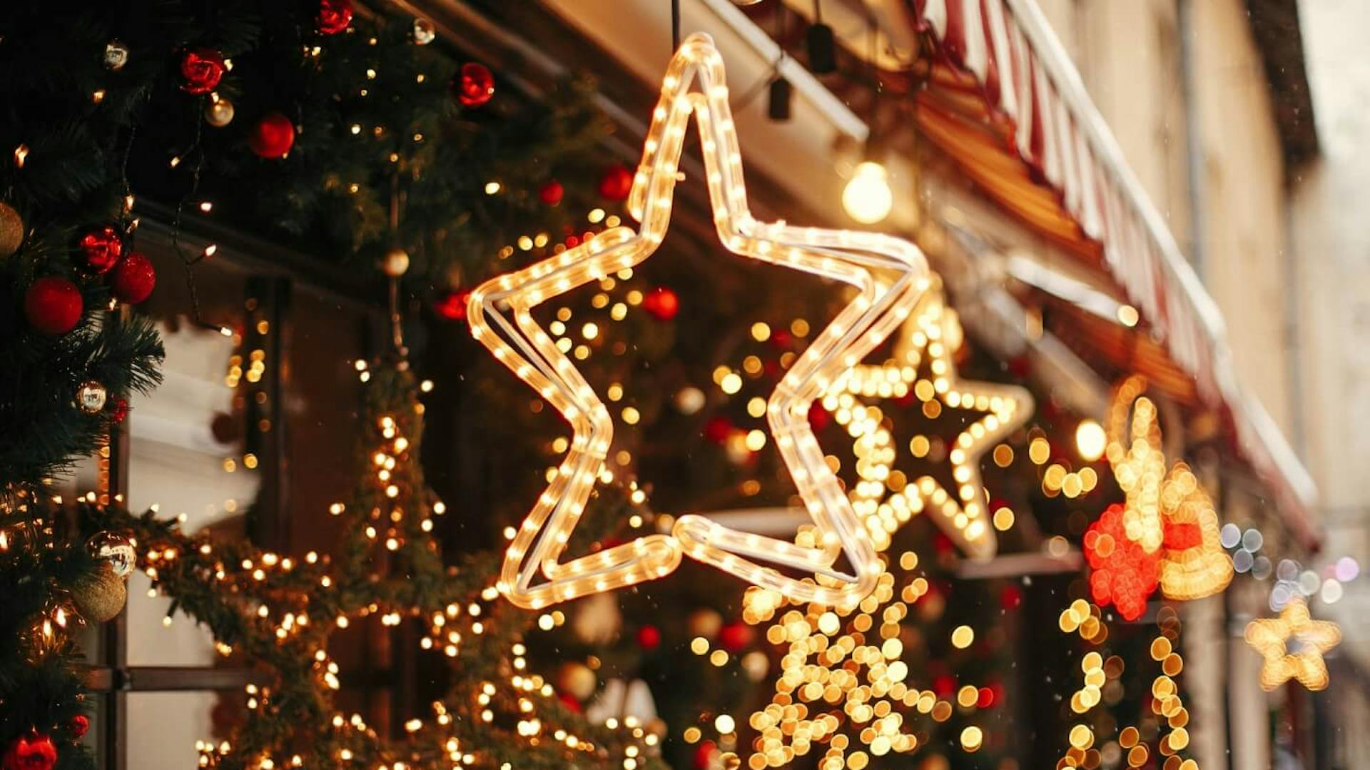 Lichterketten an Häuserfassade. An Markise hängen Lichter in Sternenform.