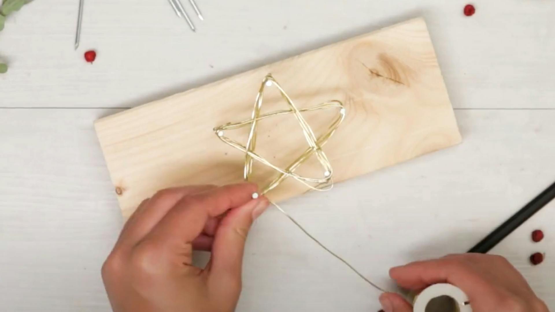 Person wickelt Draht um in Holz geschlagene Nägel in Sternform