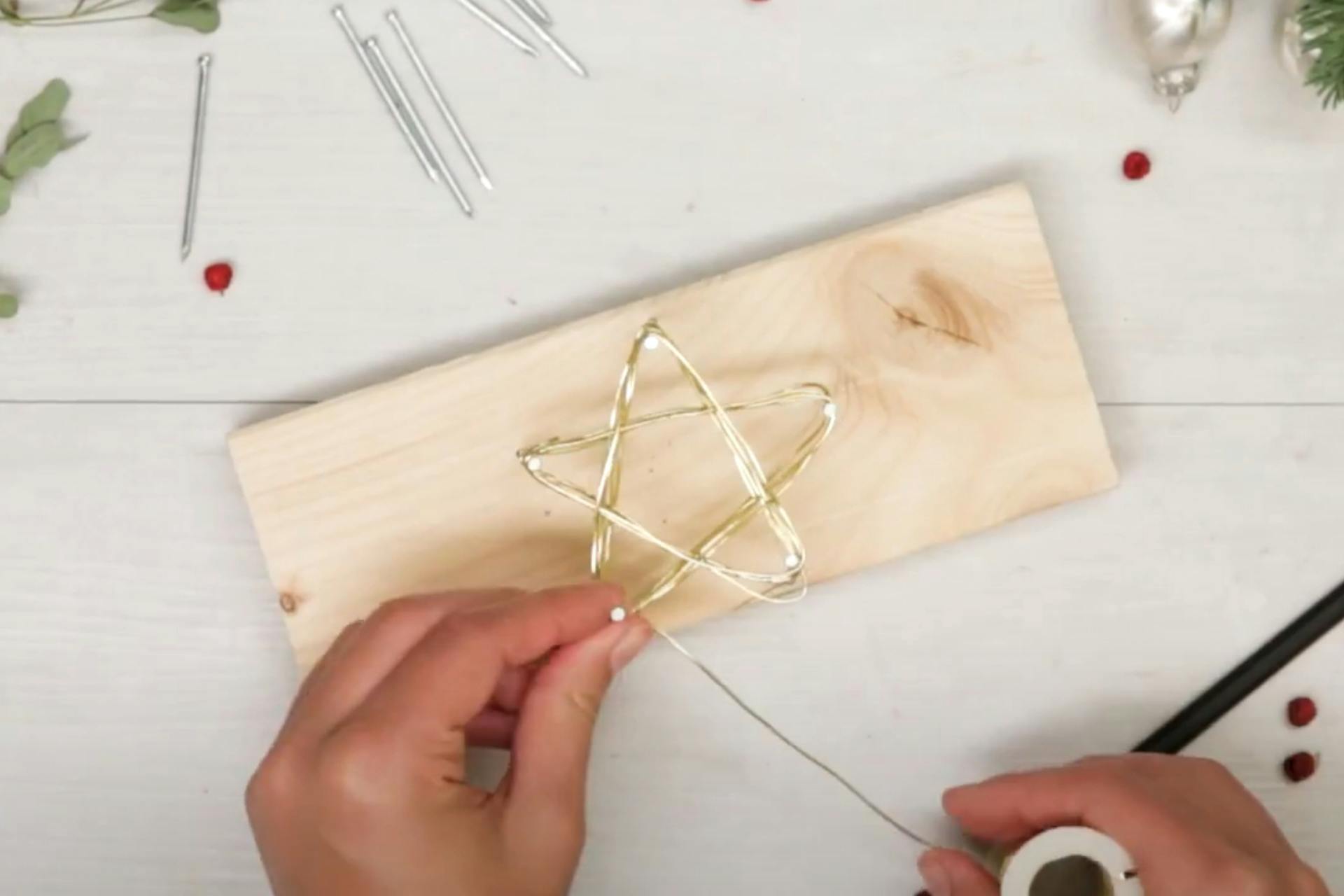 Una persona avvolge il filo metallico intorno ai chiodi inseriti nel legno disposti a forma di stella