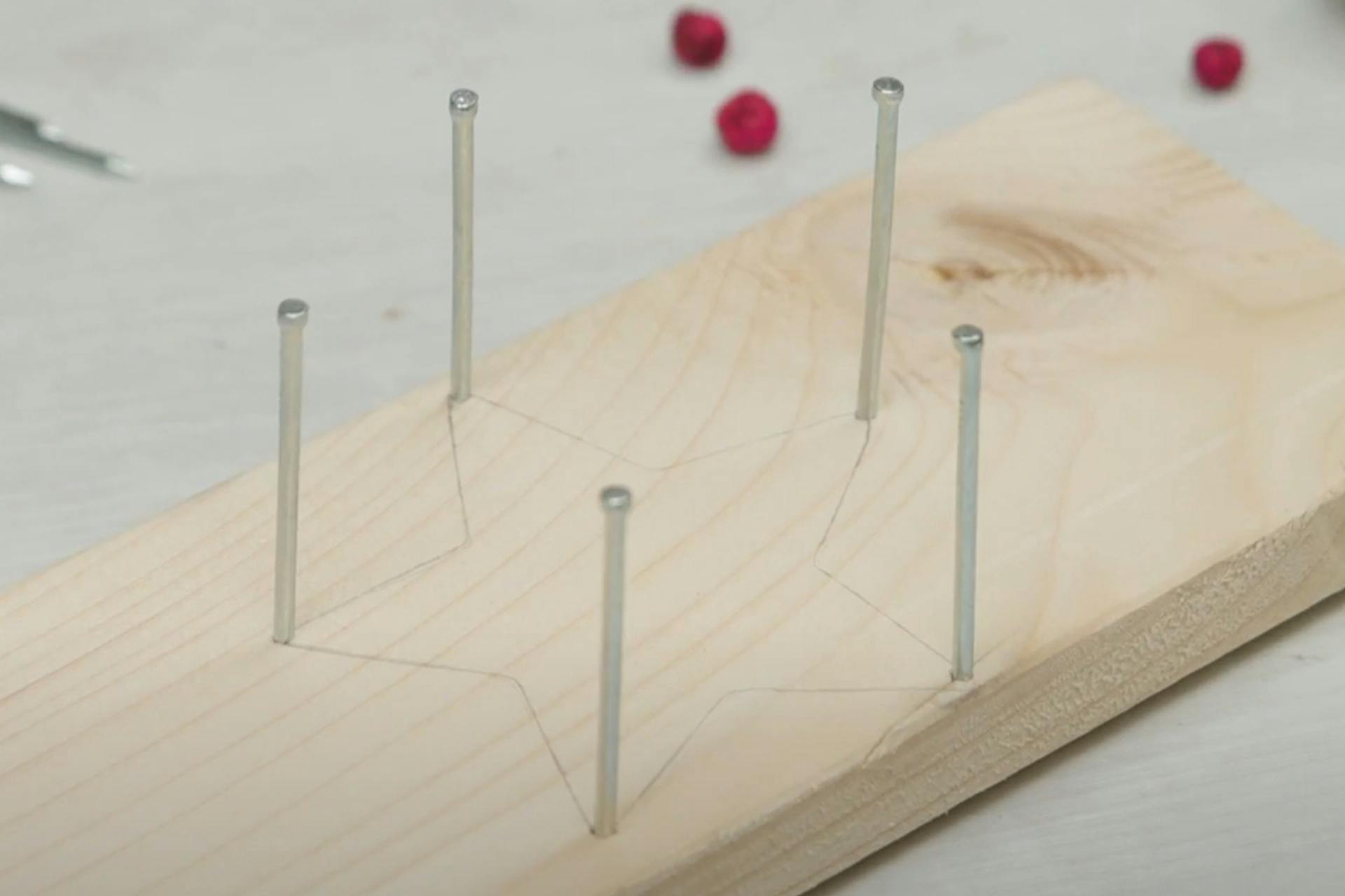 Asse di legno con la forma della stella disegnata e chiodi piantati nelle punte della stella.