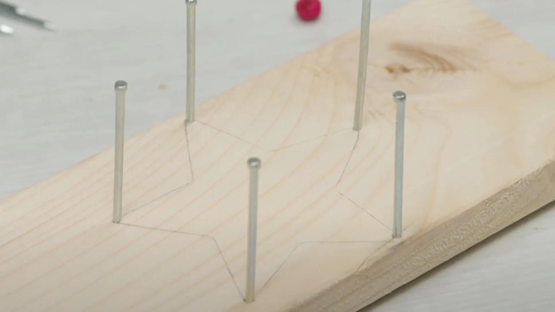Holzbrett mit aufgezeichneter Sternform und eingehämmerten Nägeln in den Sternzacken.