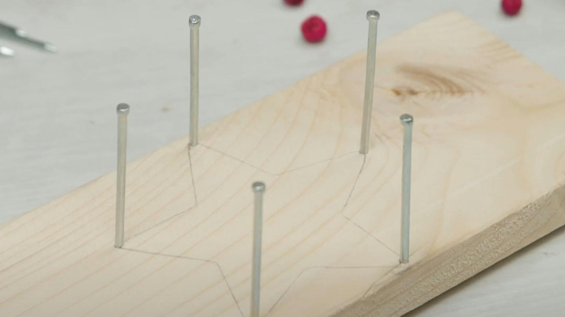 Holzbrett mit aufgezeichneter Sternform und eingehämmerten Nägeln in den Sternzacken.