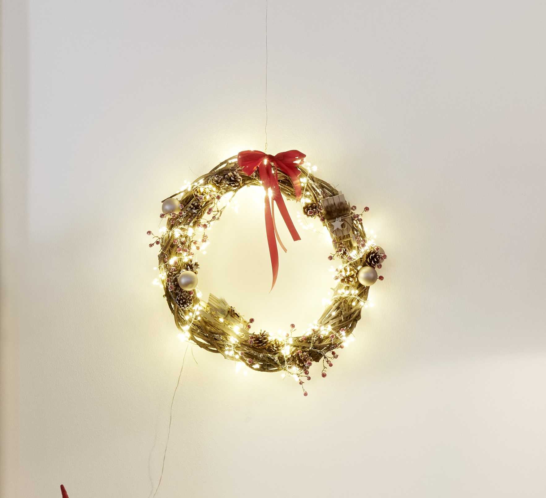 Corona con ghirlanda luminosa e fiocco come idea per decorazioni natalizie da utilizzare intorno all’albero di Natale