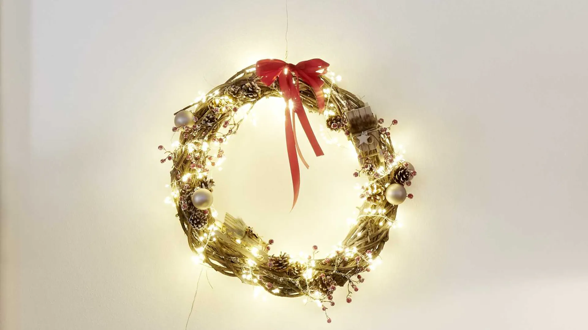 Corona con ghirlanda luminosa e fiocco come idea per decorazioni natalizie da utilizzare intorno all’albero di Natale