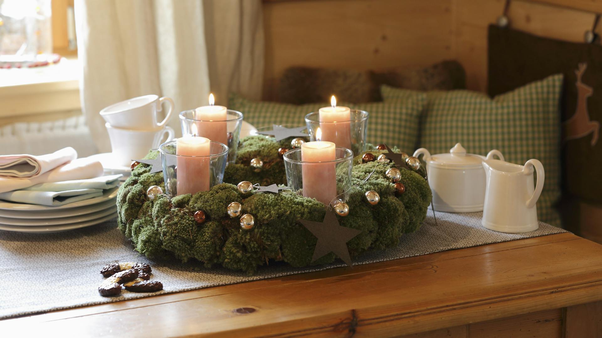 Ein Moos-Adventskranz mit Kerzen steht auf einem rustikalen Esstisch.