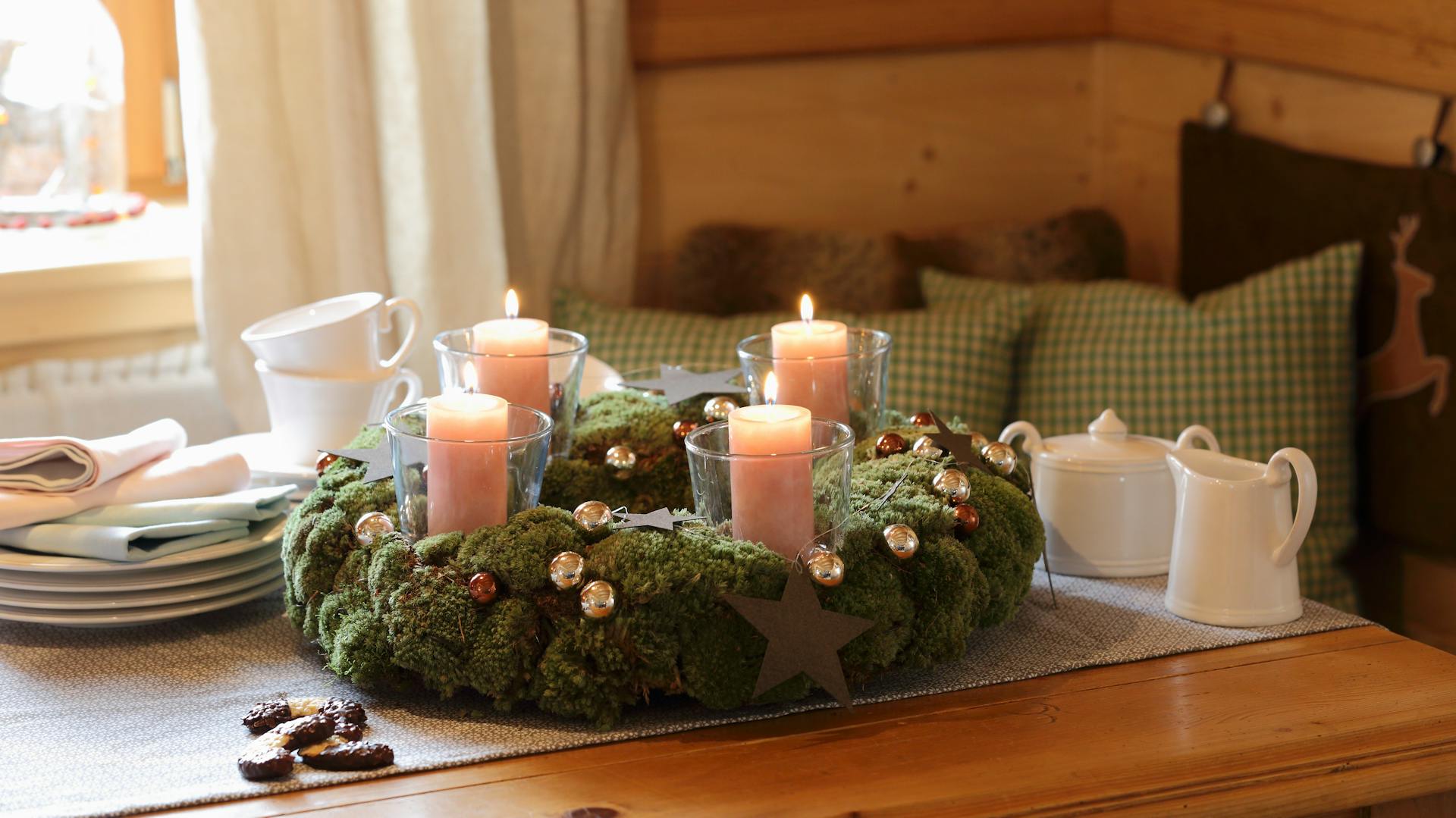 Una corona dell’Avvento in muschio con candele è disposta su un tavolo da pranzo rustico.
