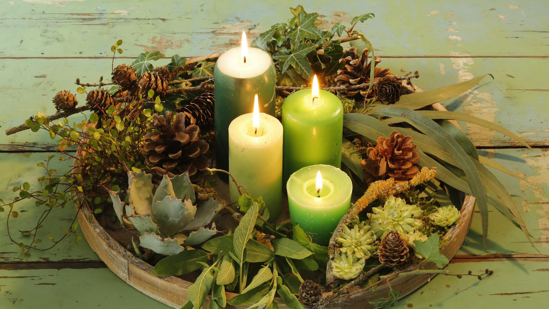 Vassoio rotondo come corona dell'Avvento con ramoscelli, materiali naturali e candele verdi accese sul tavolo