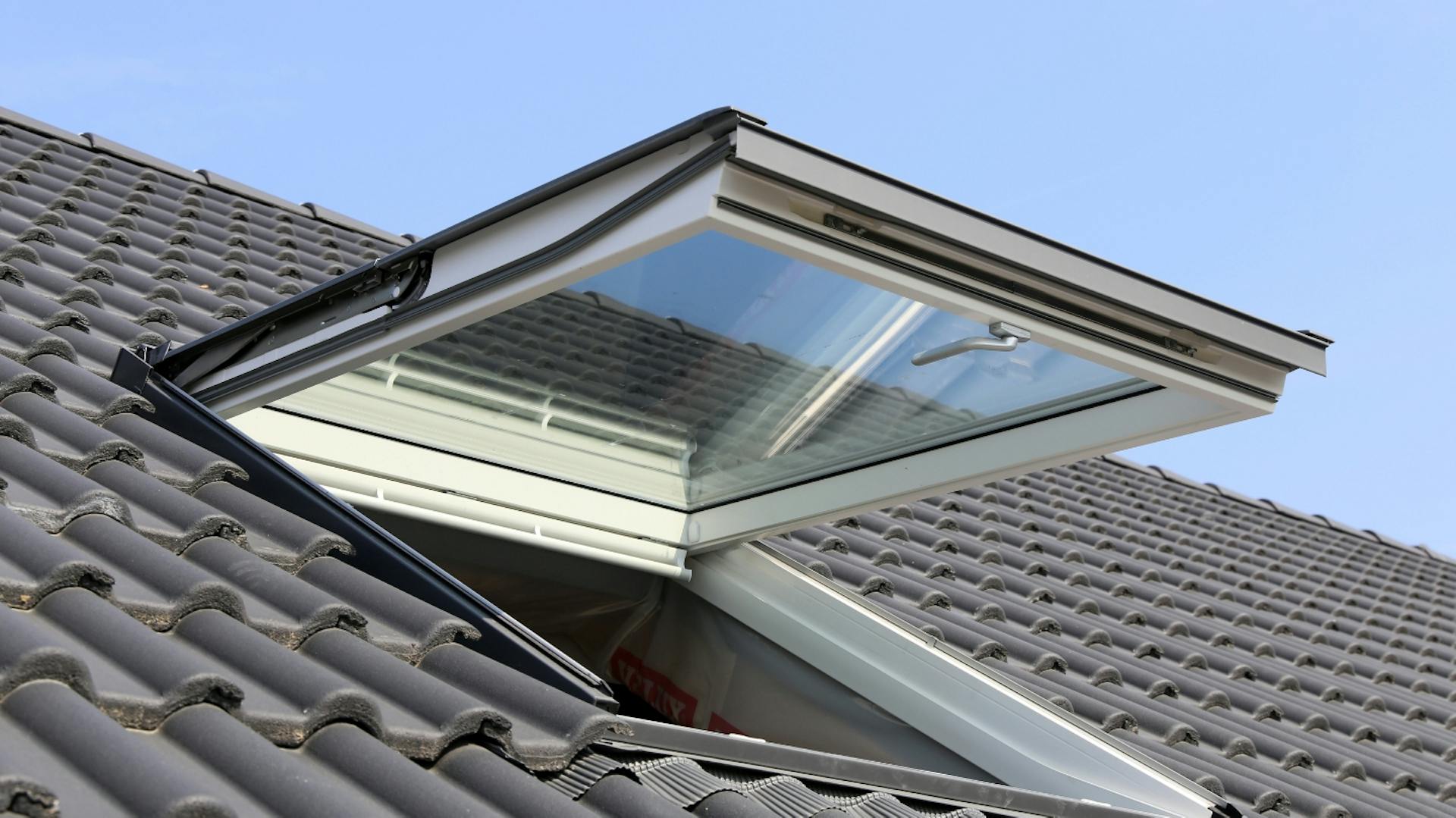 Geöffnetes Dachfenster auf grau geziegeltem Dach.