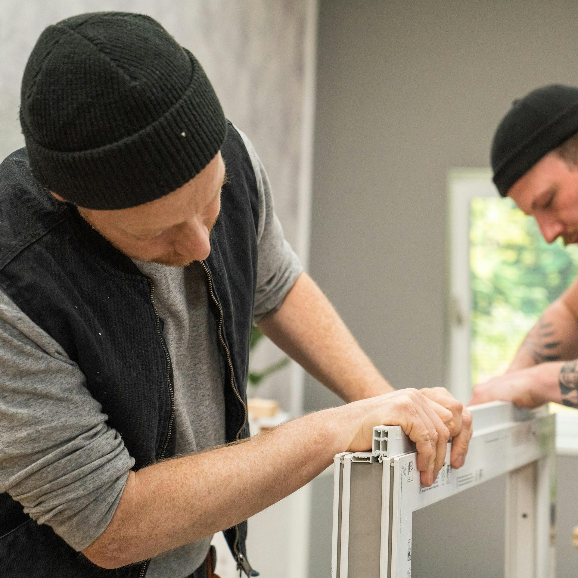 Handwerker bringen ein Fensterbankprofil am Rahmen an.