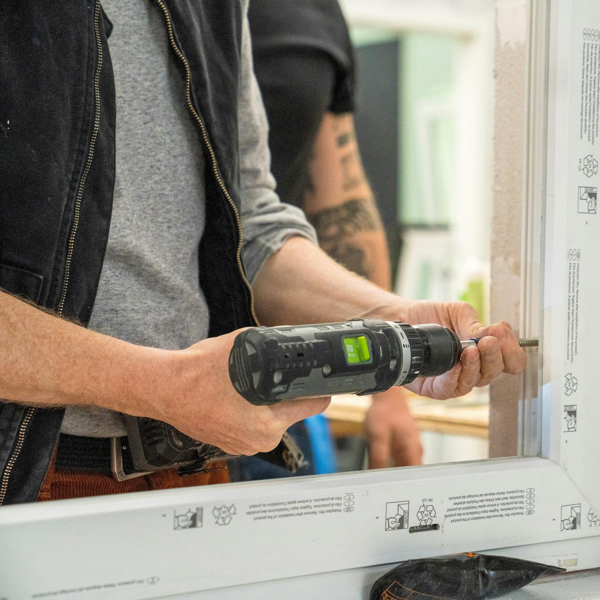 Handwerker verschraubt Fensterrahmen im Mauerwerk.