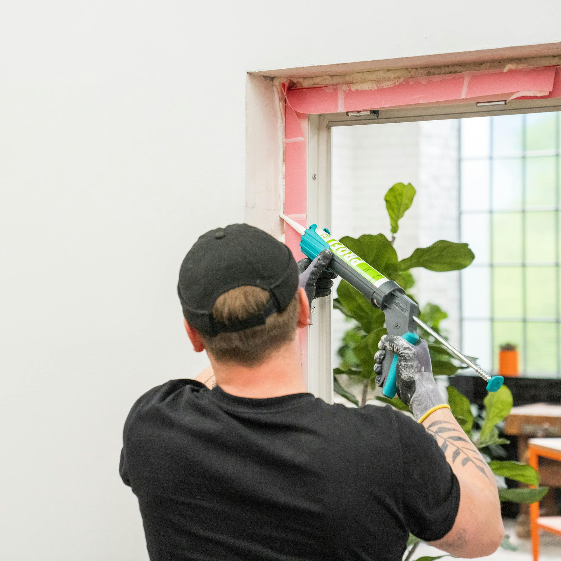 Handwerker trägt mit einer Kartuschenpistole Folienkleber auf.