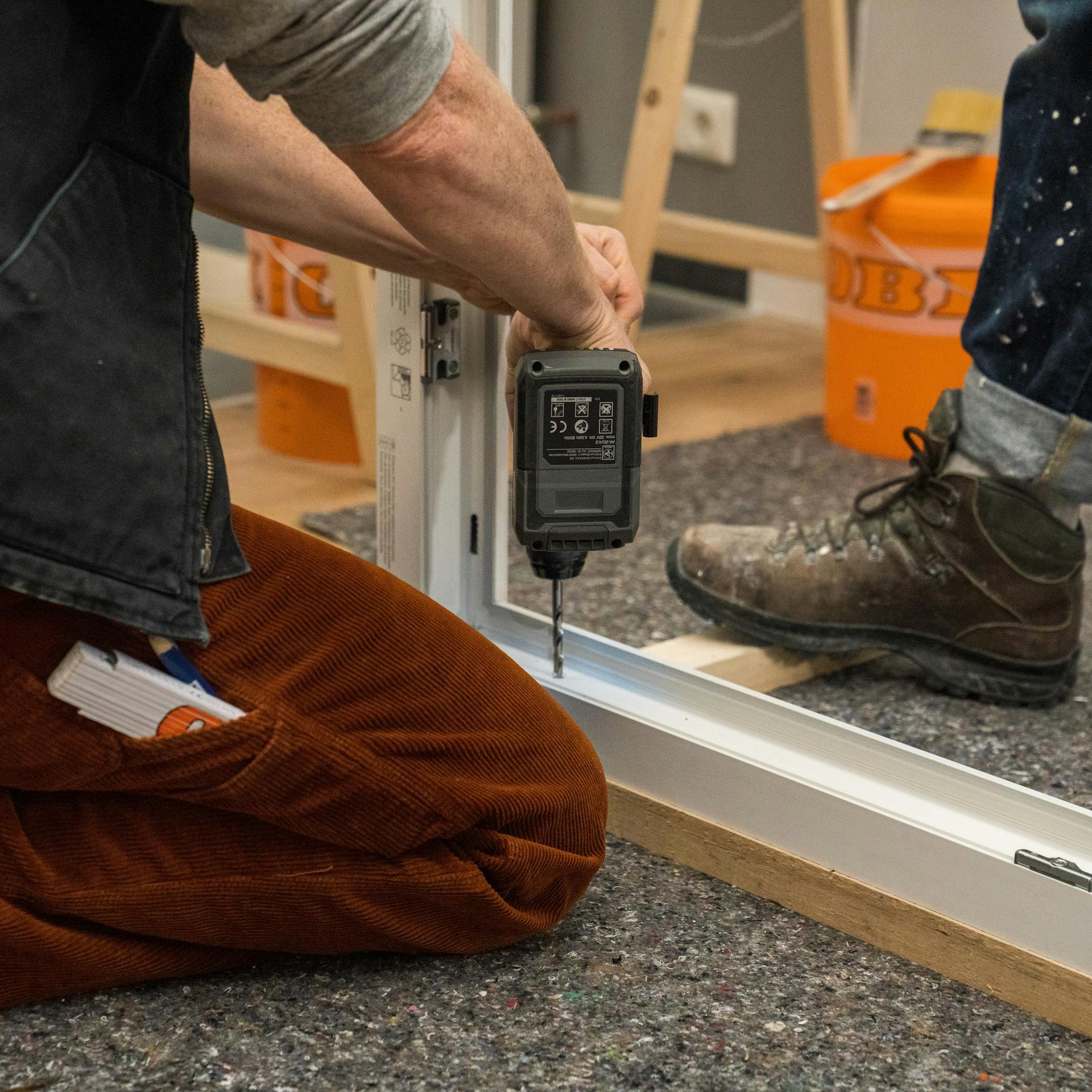 Handwerker schraubt Löcher in den Fensterrahmen.