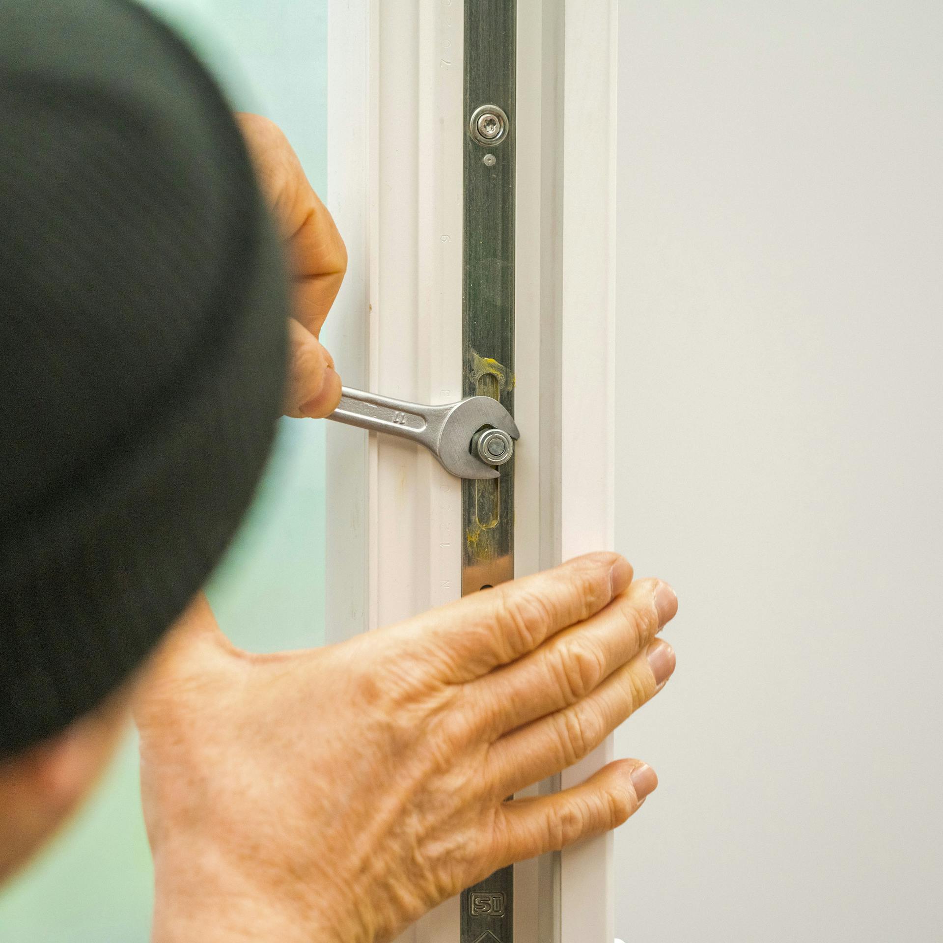 Jemand stellt den Anpressdruck eines Fensters am Schließzapfen ein.