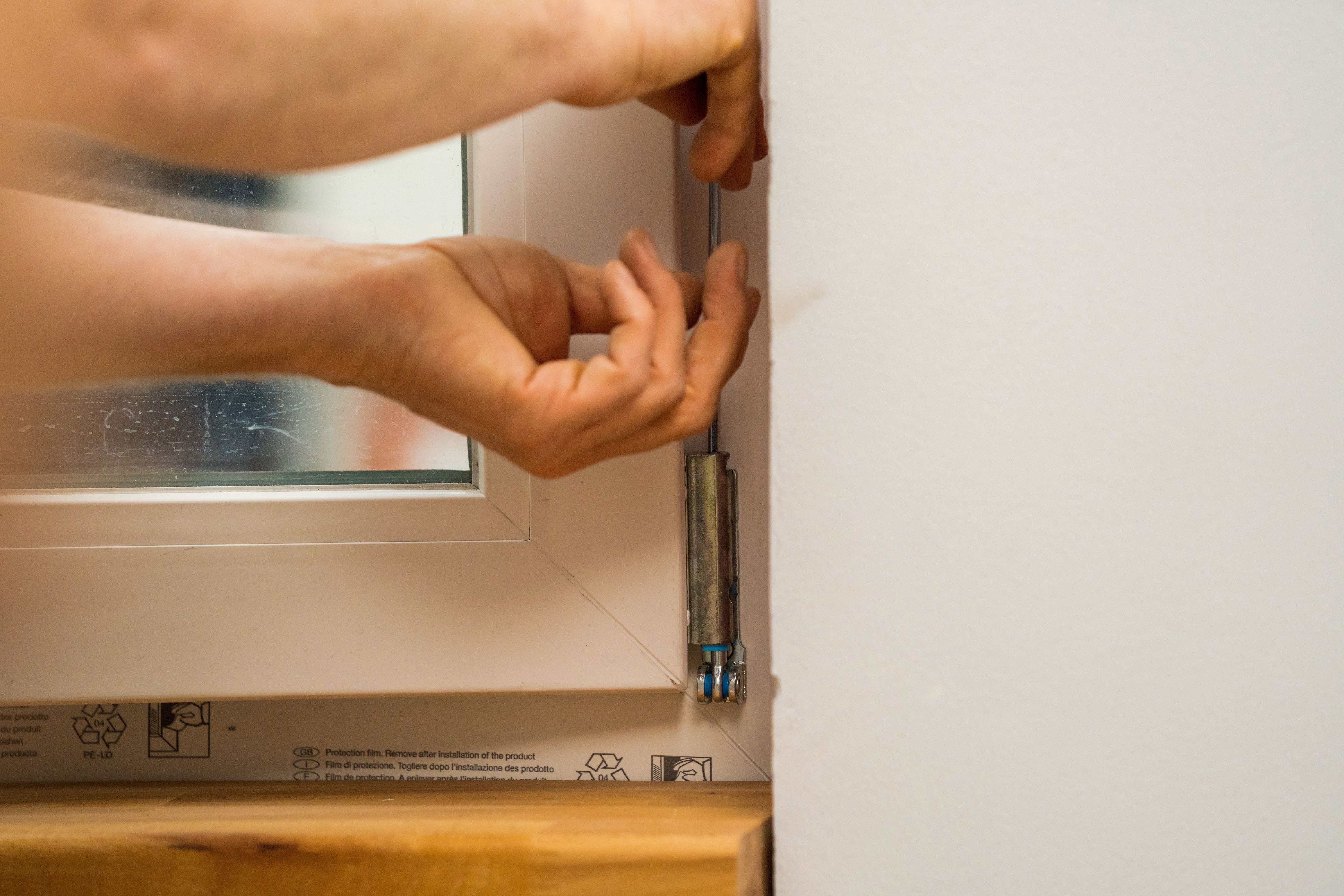 Jemand stellt einen Fensterflügel am Ecklager des Fensters ein.