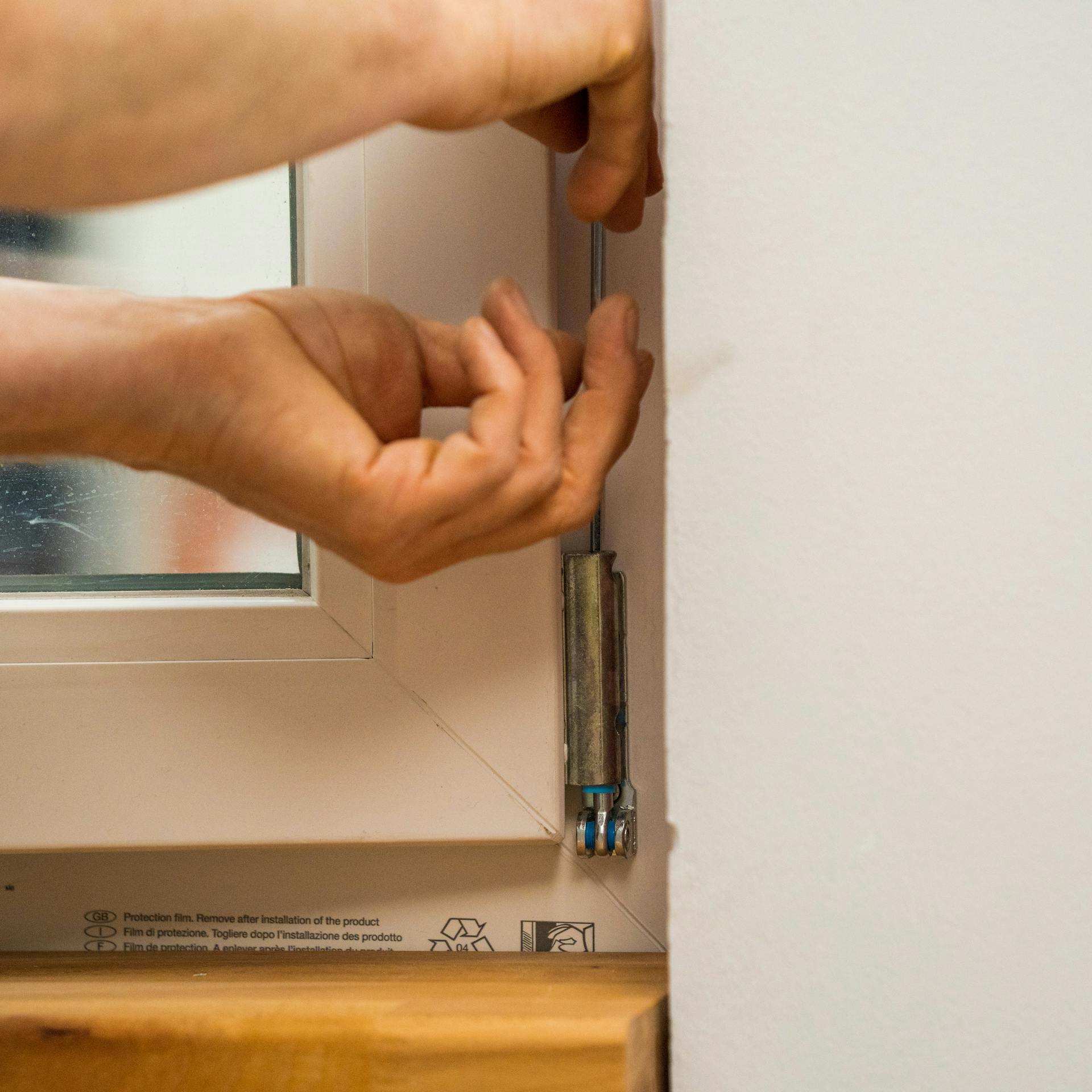 Jemand stellt einen Fensterflügel am Ecklager des Fensters ein.