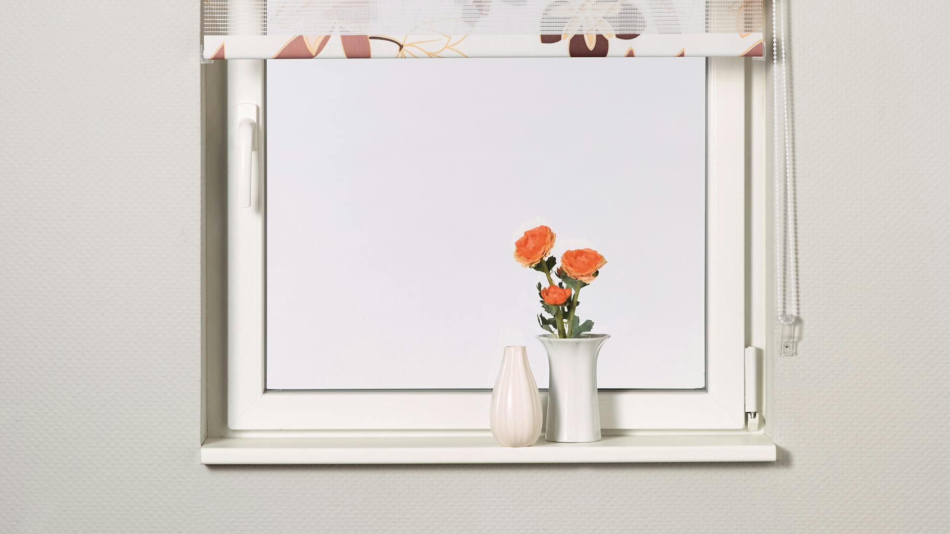 Eine weiße Fensterbank mit einer Blumenvase und geblümten Jalousien.