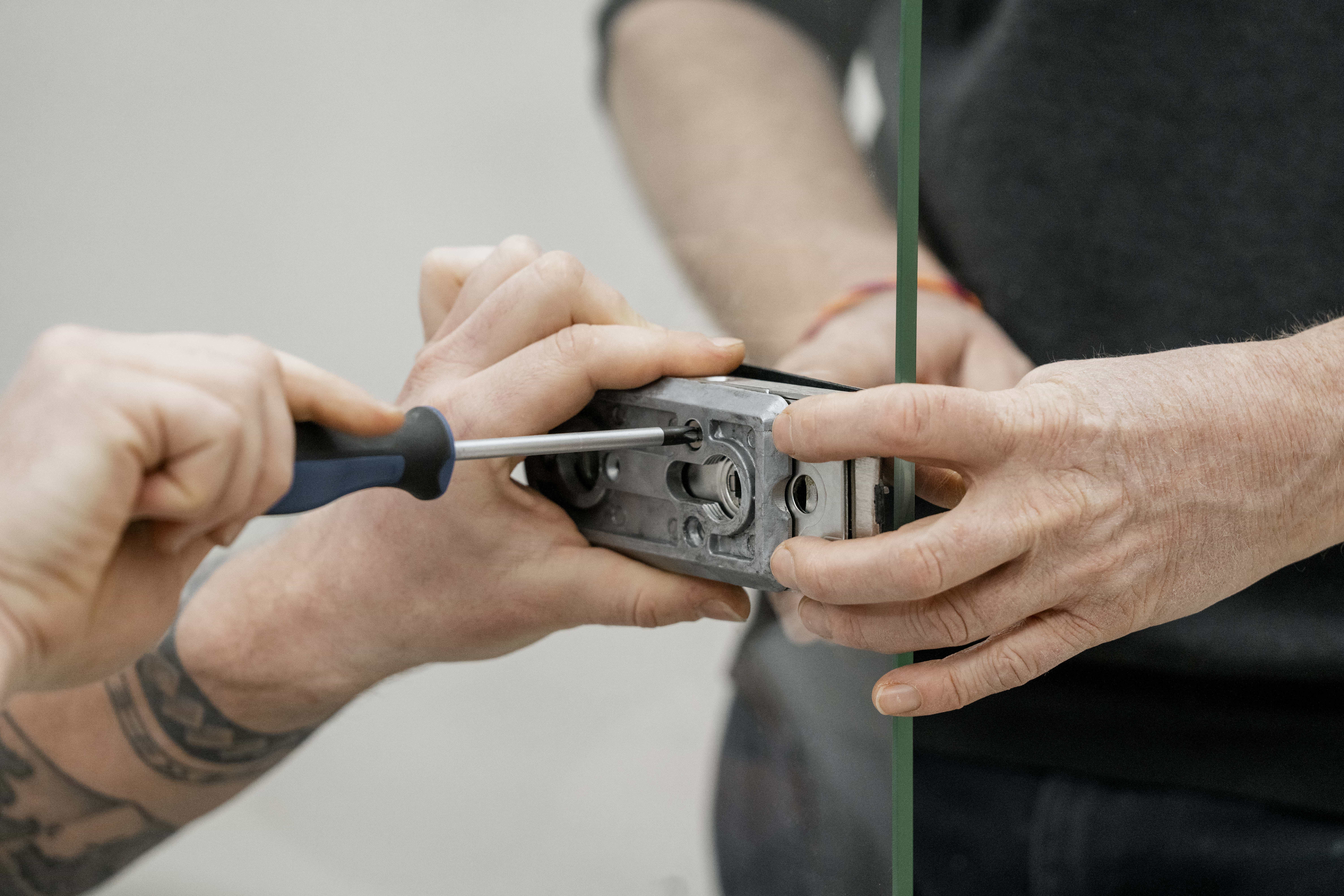 Zwei Personen montieren einen Schlosskasten an einer Glastür