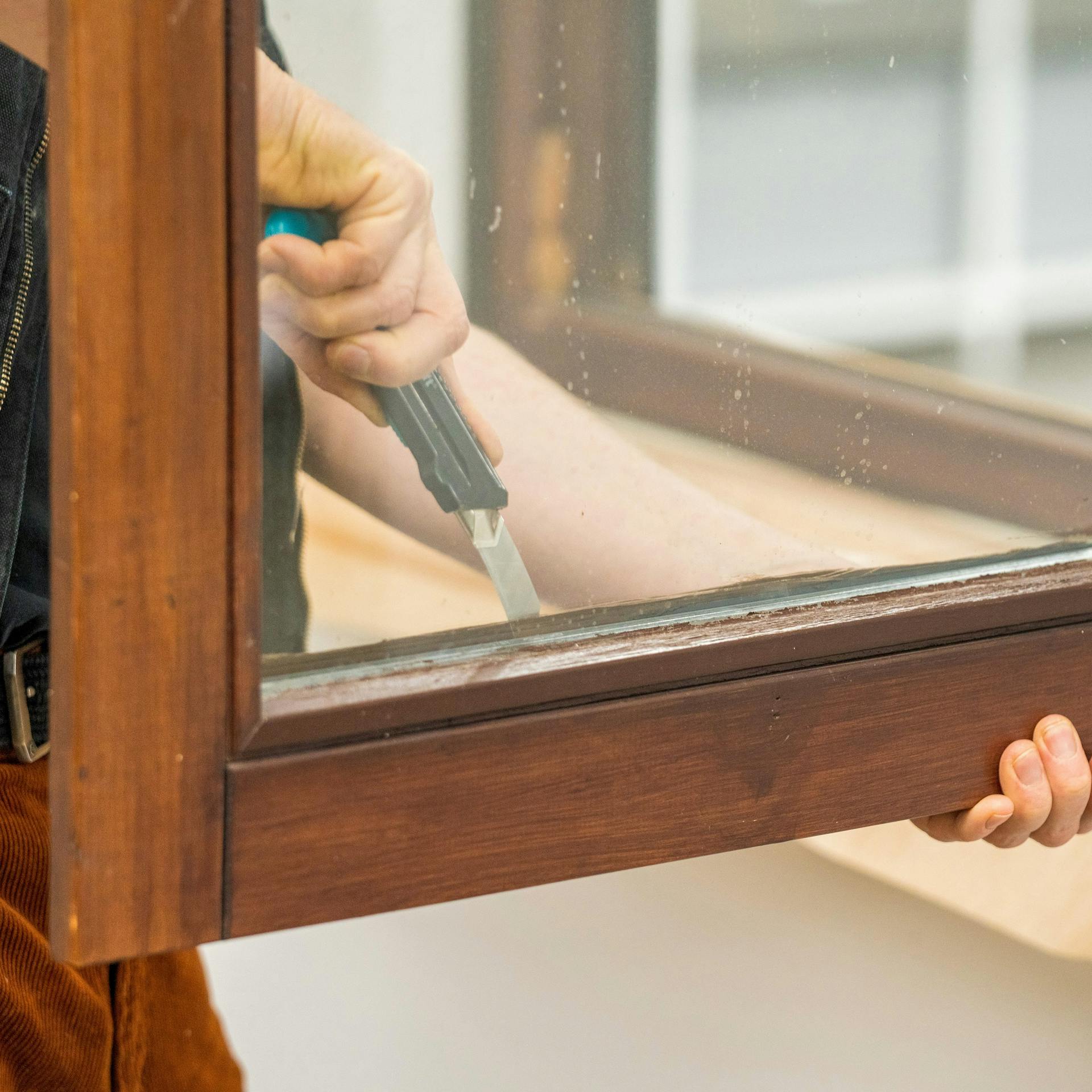Heimwerker entfernt Dichtungen an einem Holzfenster.