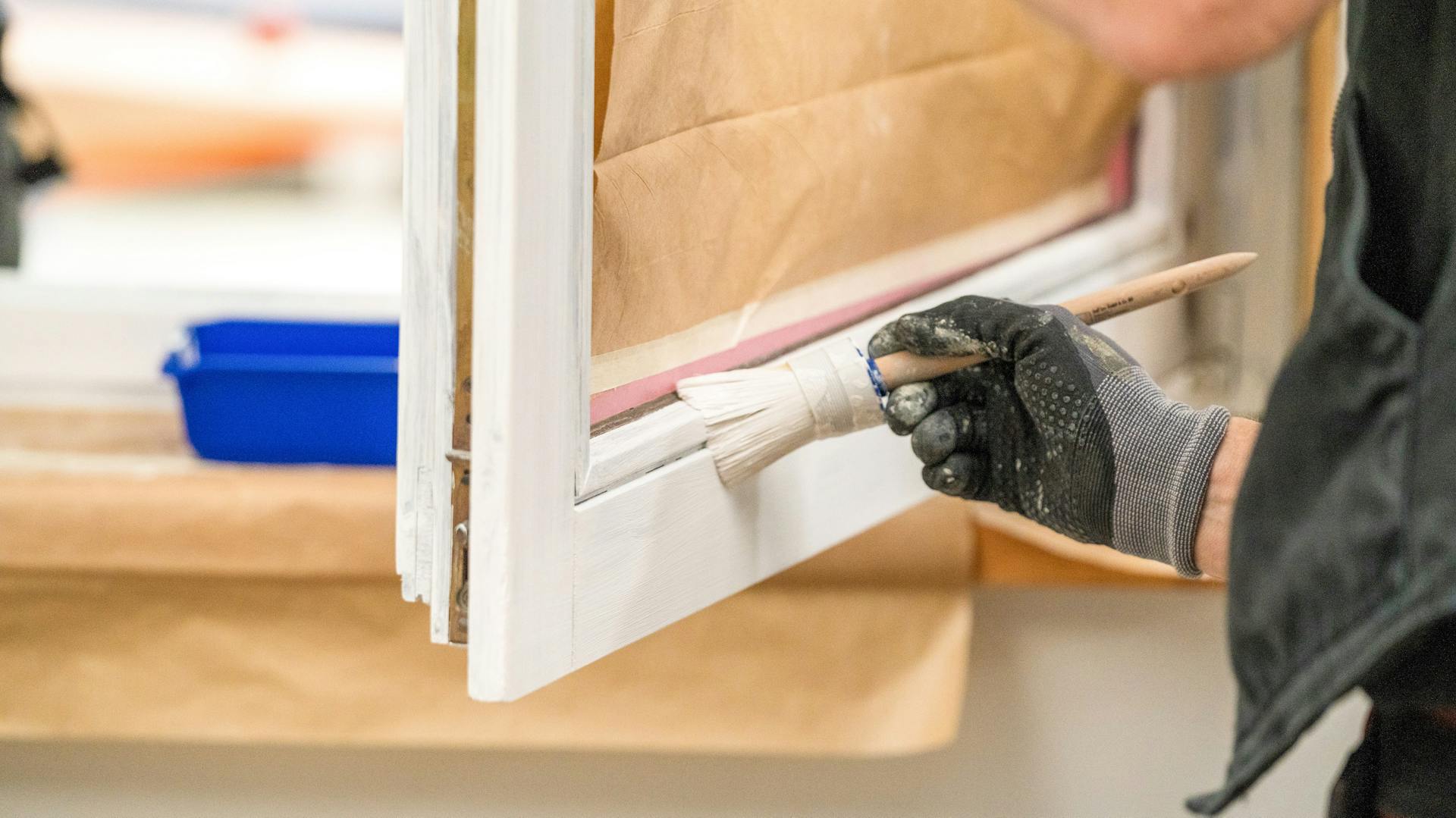 Eine Person streicht ein Fenster mit weißem Lack.