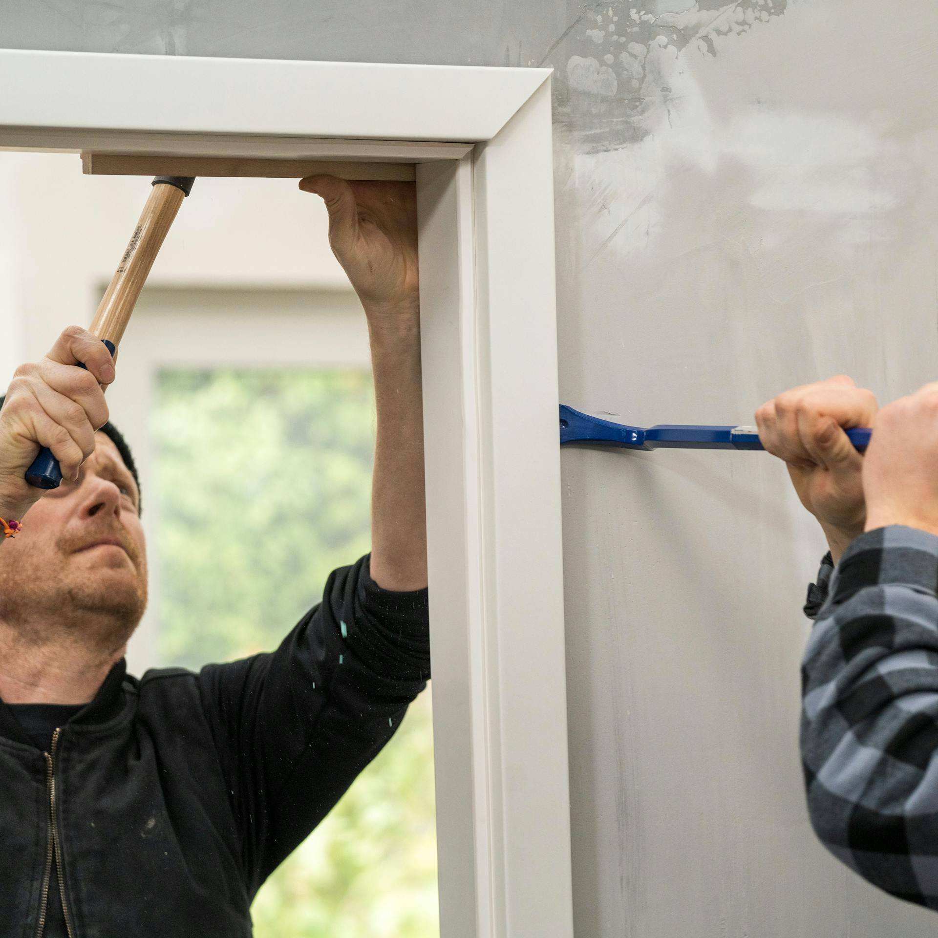 Handwerker entfernen den Rahmen einer alten Tür mit einem Hammer und Schlagholz.