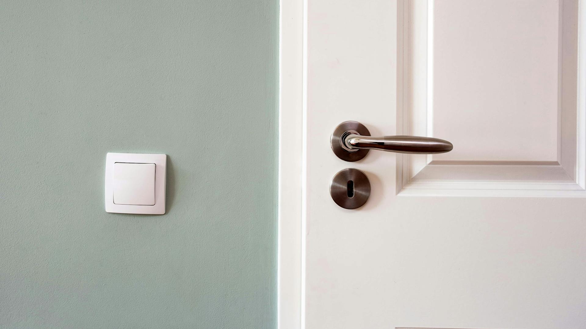 Ein Rosettenbeschlag an einer weißen Tür vor grüner Wand.