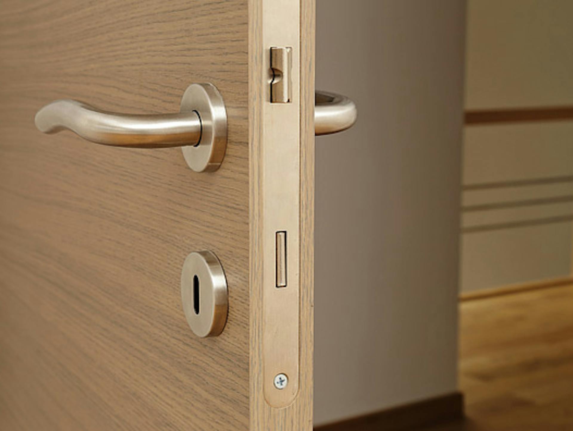 Geöffnete Tür mit Türklinken und Schlüsselloch, die den Blick auf ein Treppengelände freigibt.