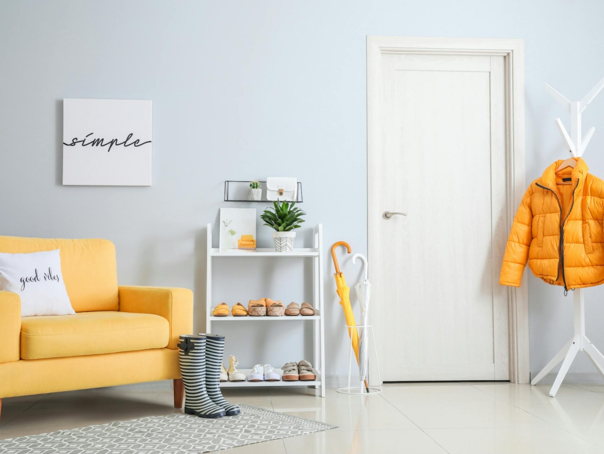 Zimmer mit gelber Couch und Garderobe. In der Mitte eine Weißlack-Tür