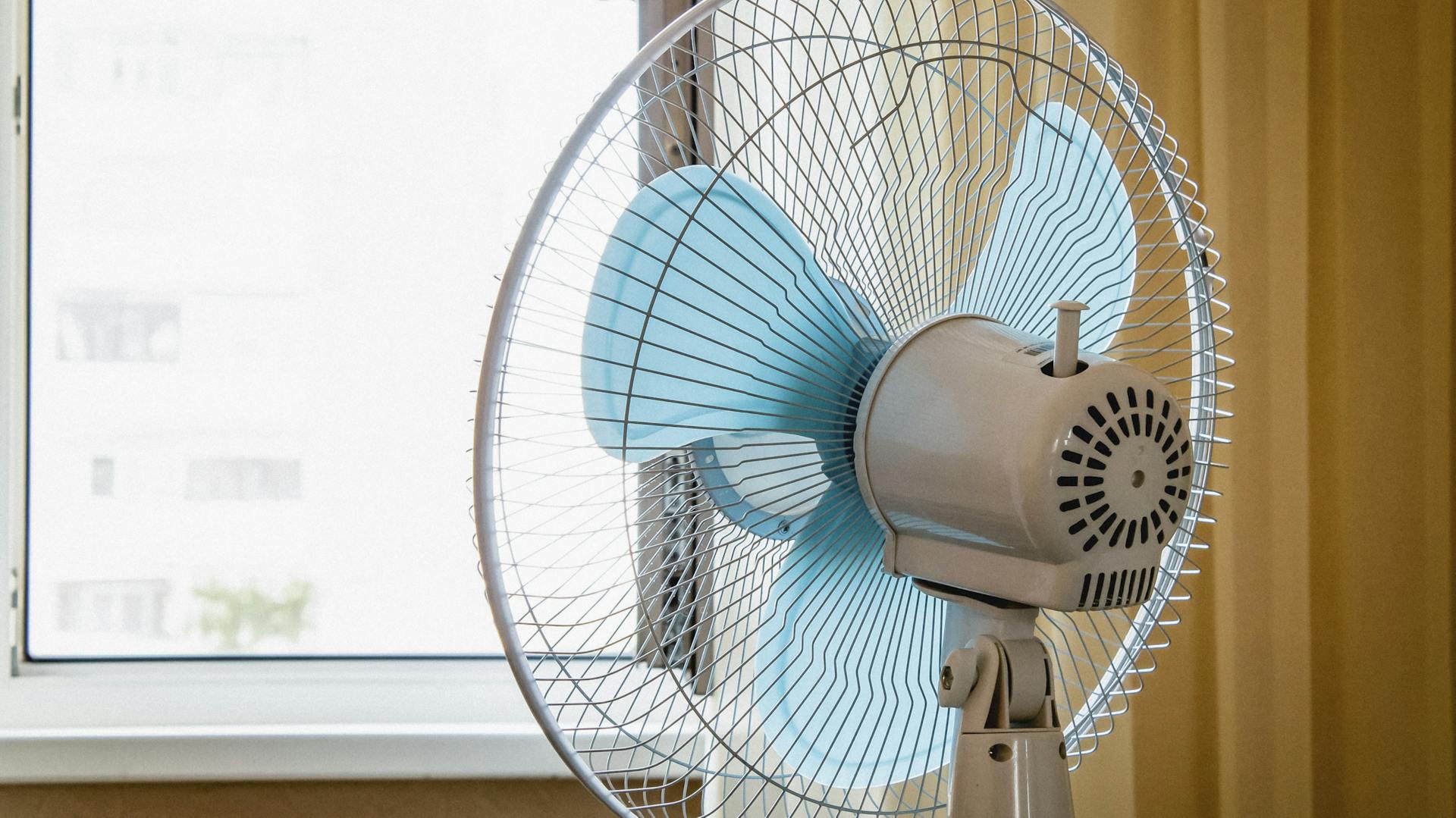 Ein Standventilator pustet die warme Luft aus der Wohnung aus dem offenen Fenster