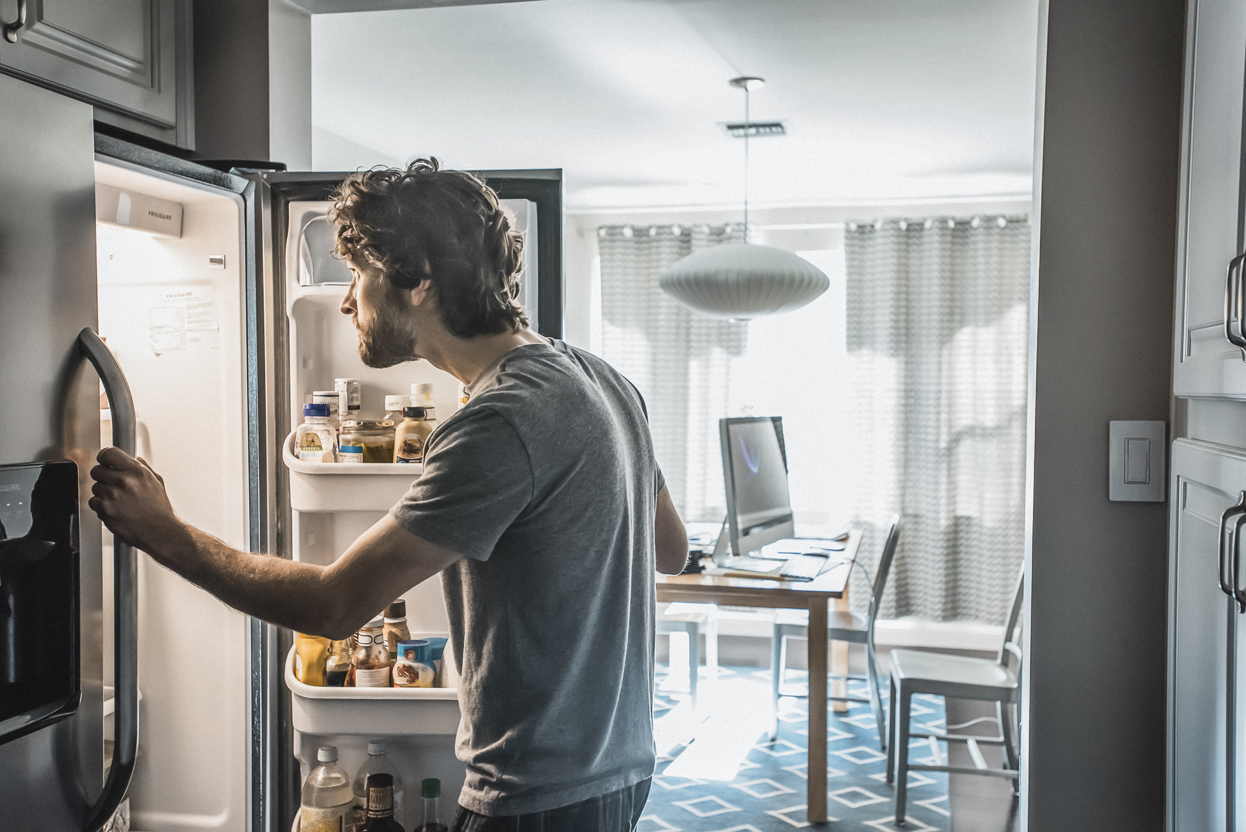 Un uomo guarda dentro a un frigorifero, sullo sfondo il suo home office