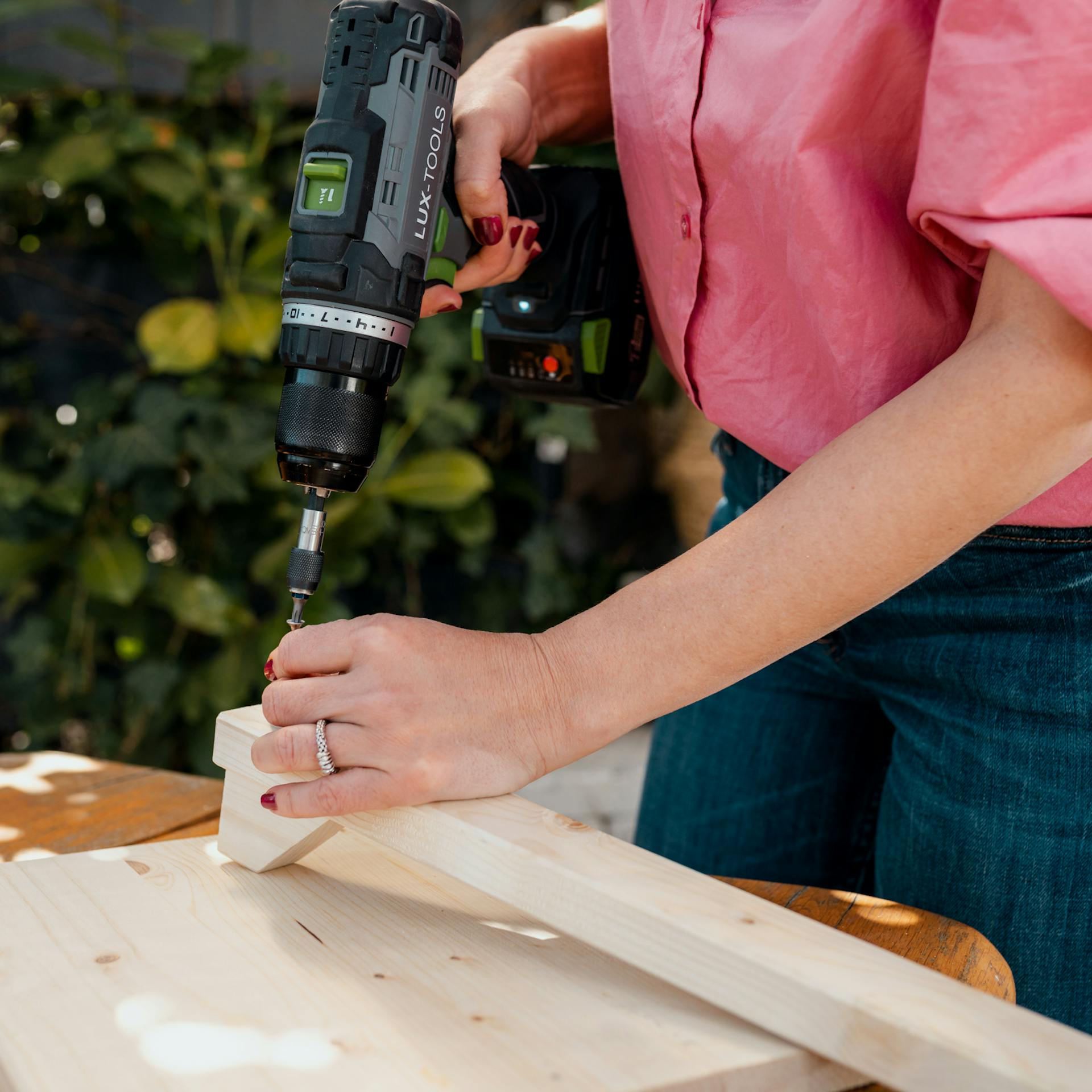 Frau dreht eine Schraube mit einem Akkuschrauber in eine Holzlatte