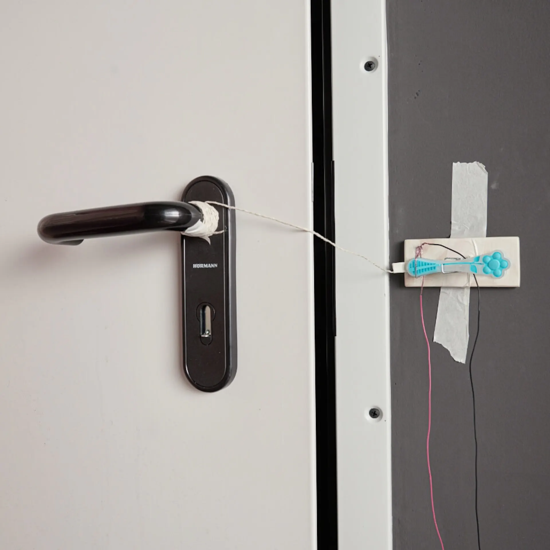 Holzbrett mit Wäscheklammer ist mit Klebeband an Wand neben Tür befestigt