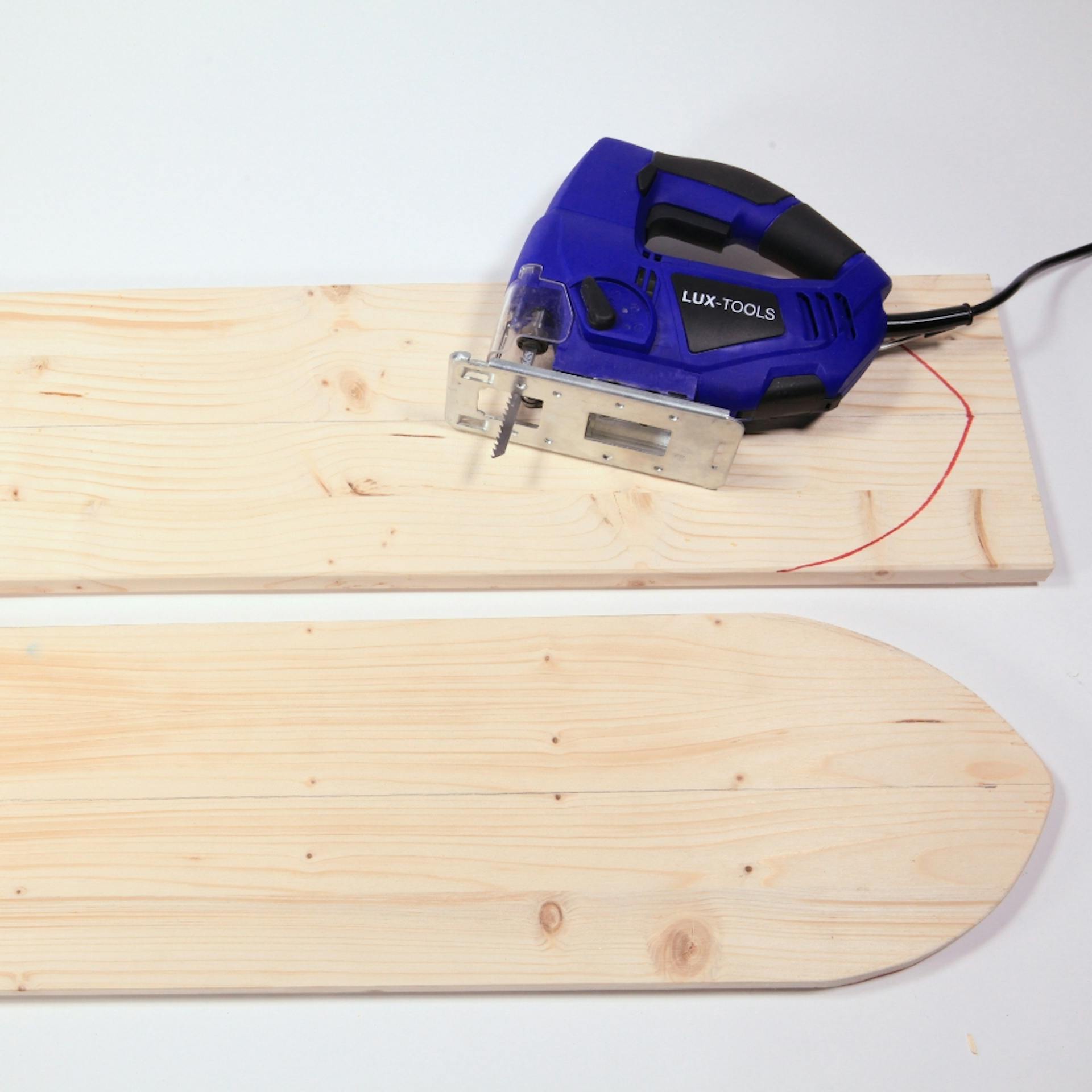 Holzbrett mit vorgezeichneter Form, darauf eine Stichsäge. Daneben liegt ein bereits ausgesägtes Balance Board.