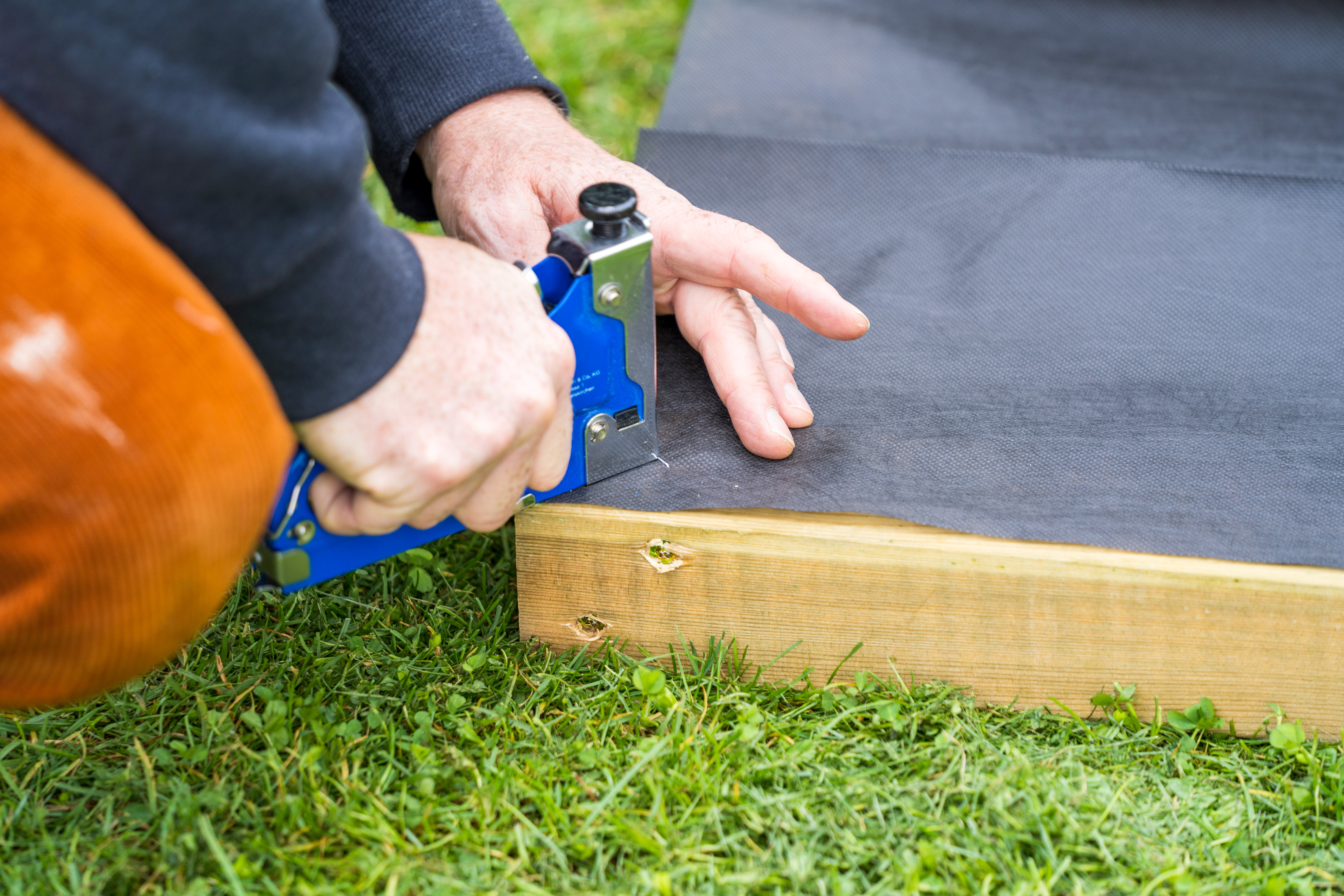 Unkrautvlies wird an Rückseite von Rahmen des Barfußpfades befestigt