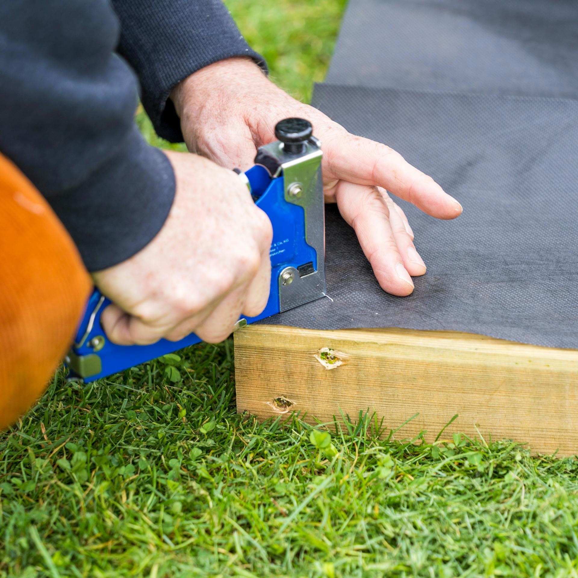 Unkrautvlies wird an Rückseite von Rahmen des Barfußpfades befestigt