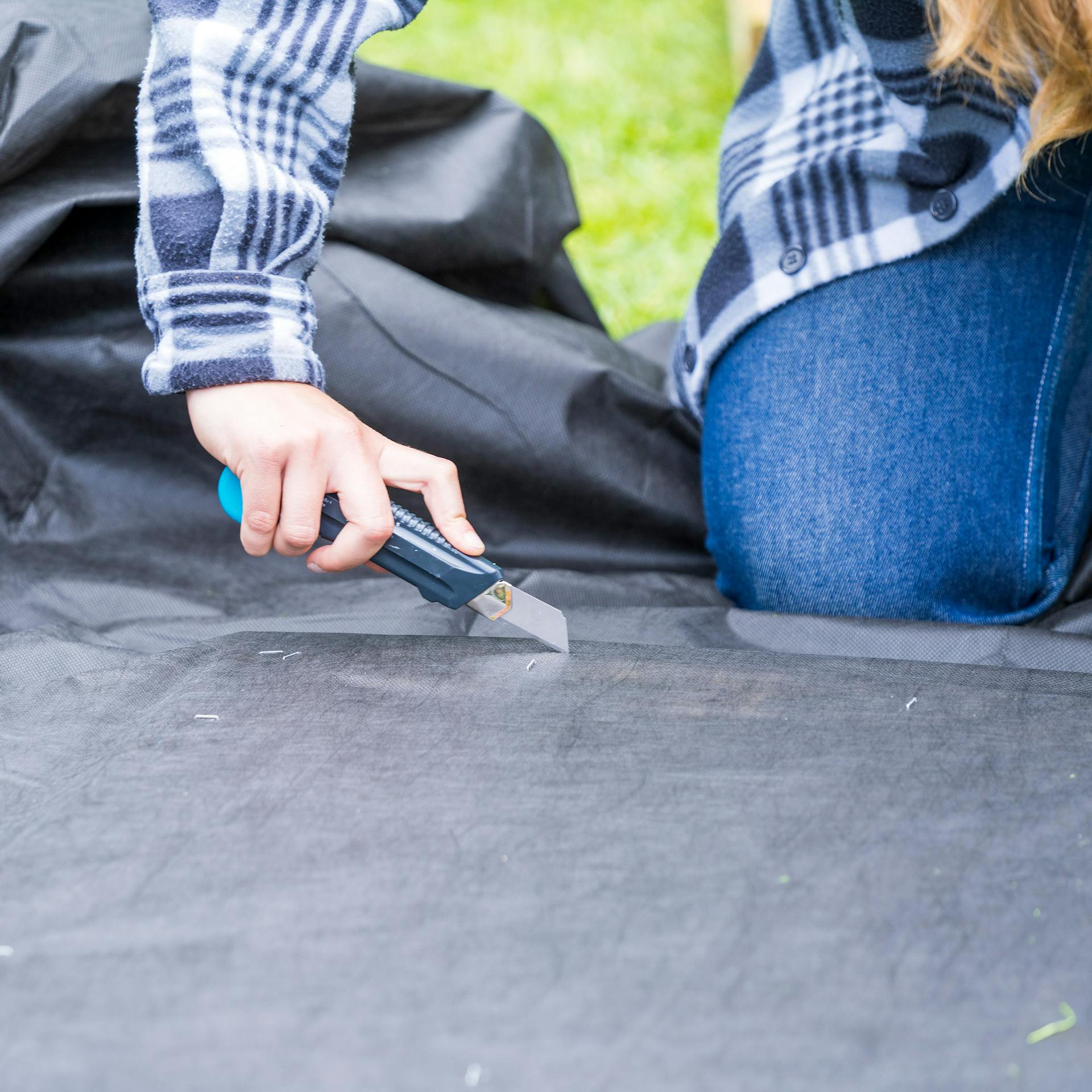 Überstehendes Unkrautvlies wird mit Cuttermesser gekürzt