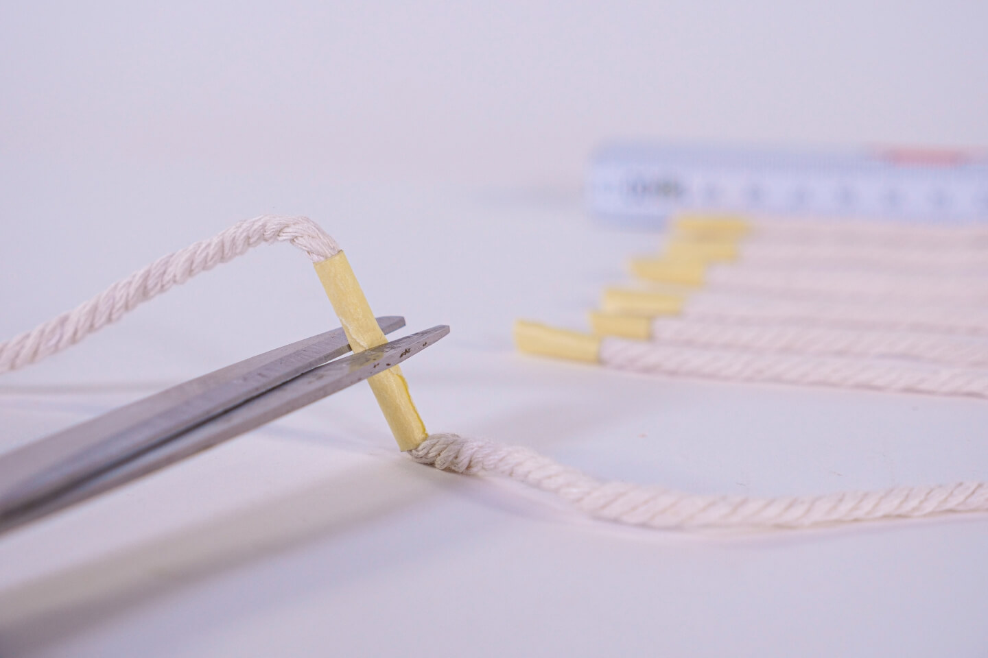 Egy szál makramé fonalat vágnak le ollóval. Egy darab ragasztószalag szolgál jelölőként.