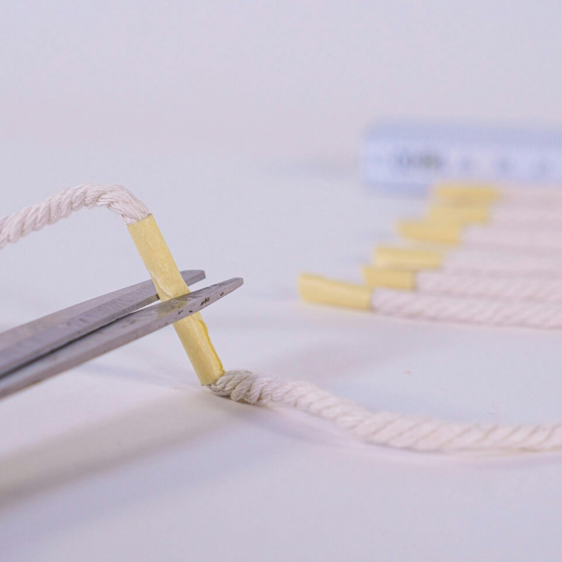 Egy szál makramé fonalat vágnak le ollóval. Egy darab ragasztószalag szolgál jelölőként.