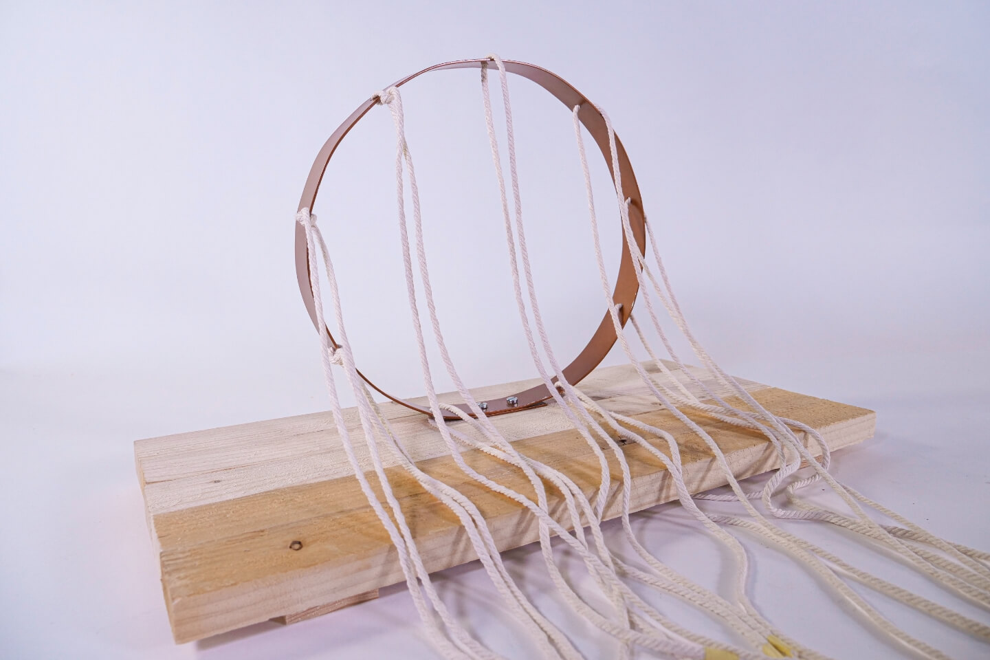 Fadeszkára csavarozott alumíniumgyűrű. Csomózatlan makramé fonal lóg rajta. 