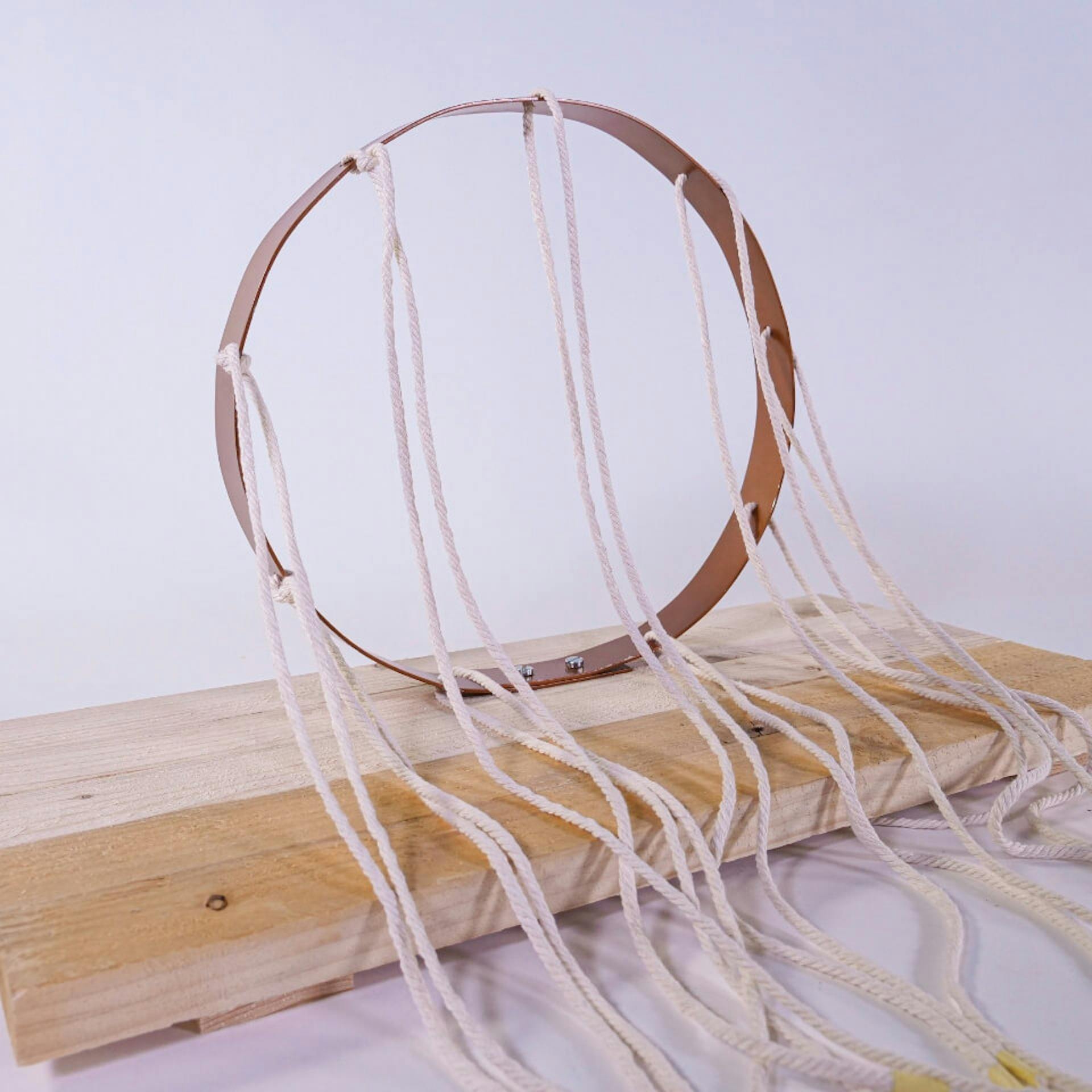 Fadeszkára csavarozott alumíniumgyűrű. Csomózatlan makramé fonal lóg rajta.