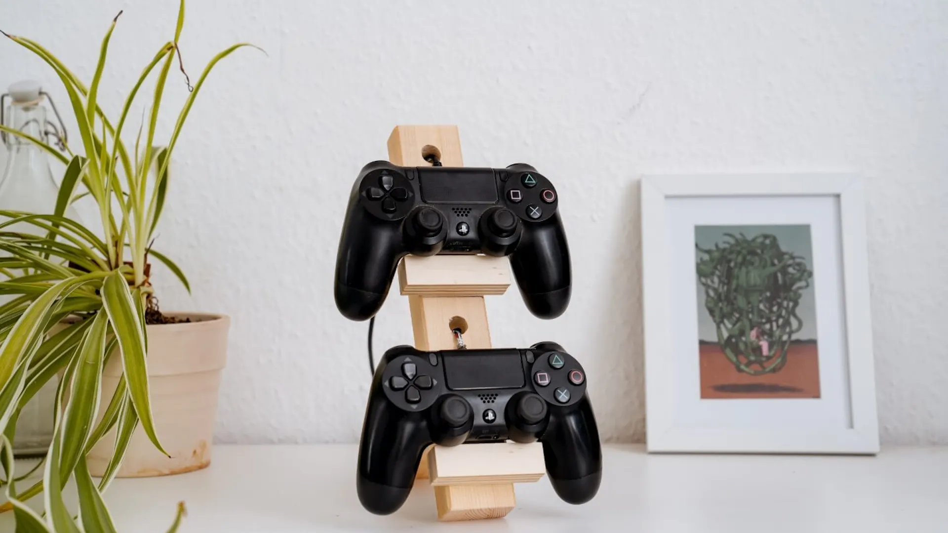 Der Controllerstand steht auf einem weißen Board. Daneben stehen eine Zimmerpflanze und ein Bild.