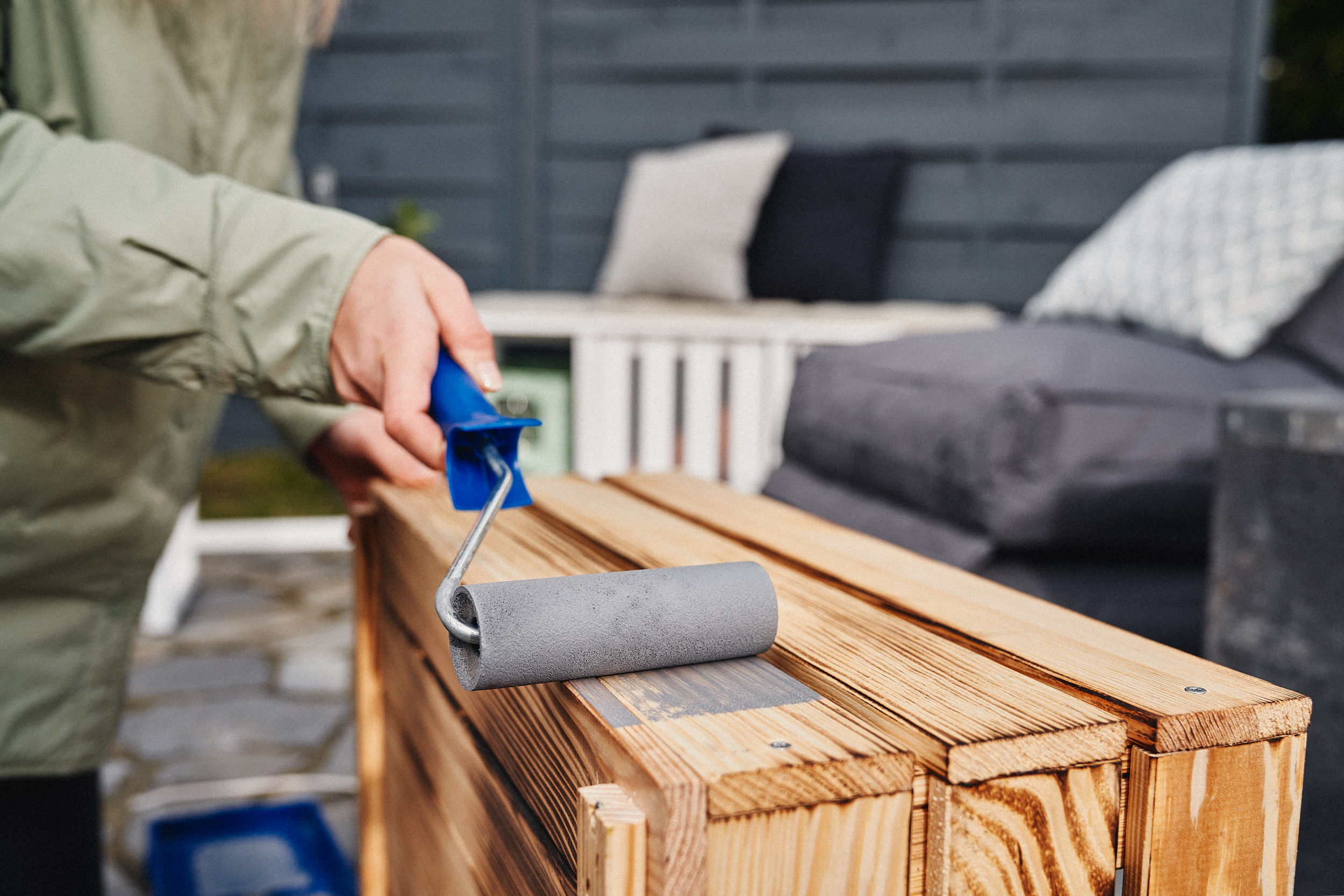 Egy lakkozó hengerrel szürke festéket visznek fel a ládára.