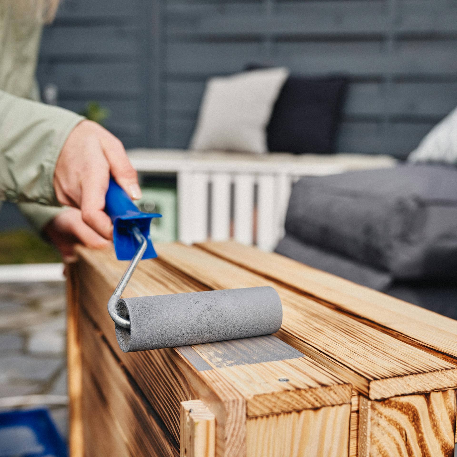 Egy lakkozó hengerrel szürke festéket visznek fel a ládára.
